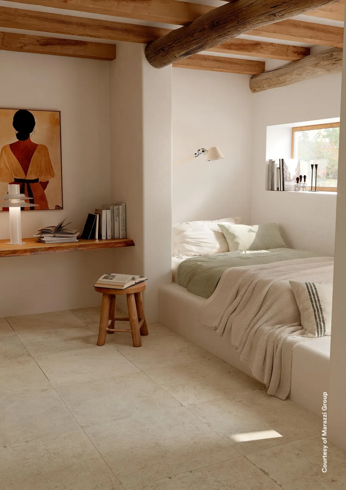 Schlafzimmer mit gemauertem Bett, Schreibplatz und cremefarbenen Steinoptik-Bodenfliesen unter einer Holzdecke