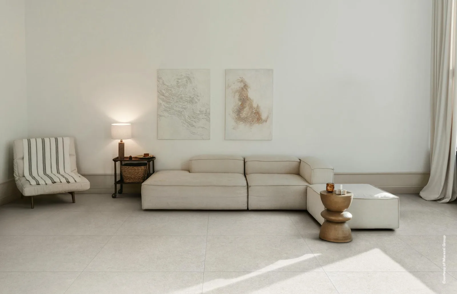 Heller Wohnraum mit beiger Steinoptik-Fliese im Großformat, helles Sofa, Sessel und zwei Bilder an der weißen Wand.
