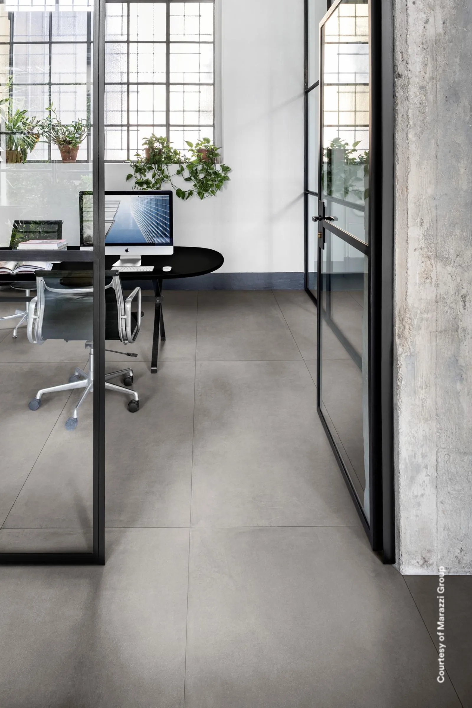 Loft-Büro mit Sprossenfenstern, Glaswänden und Schreibtisch auf mittelgrauem Betonoptik-Boden im Großformat.