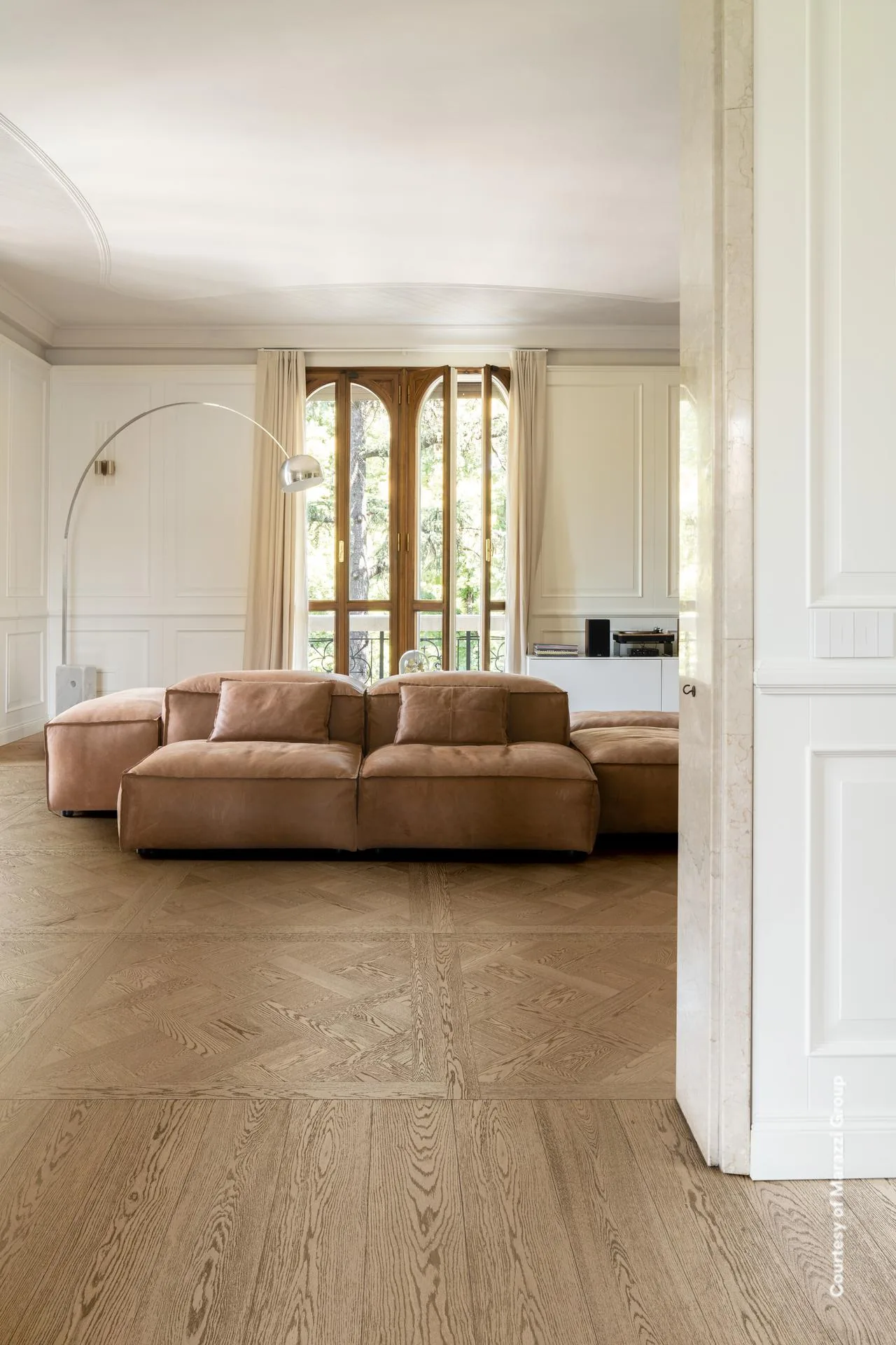 Wohnraum mit modularem Ledersofa und weißen Paneelwänden über mittelbraunen Dielen in Holzoptik.
