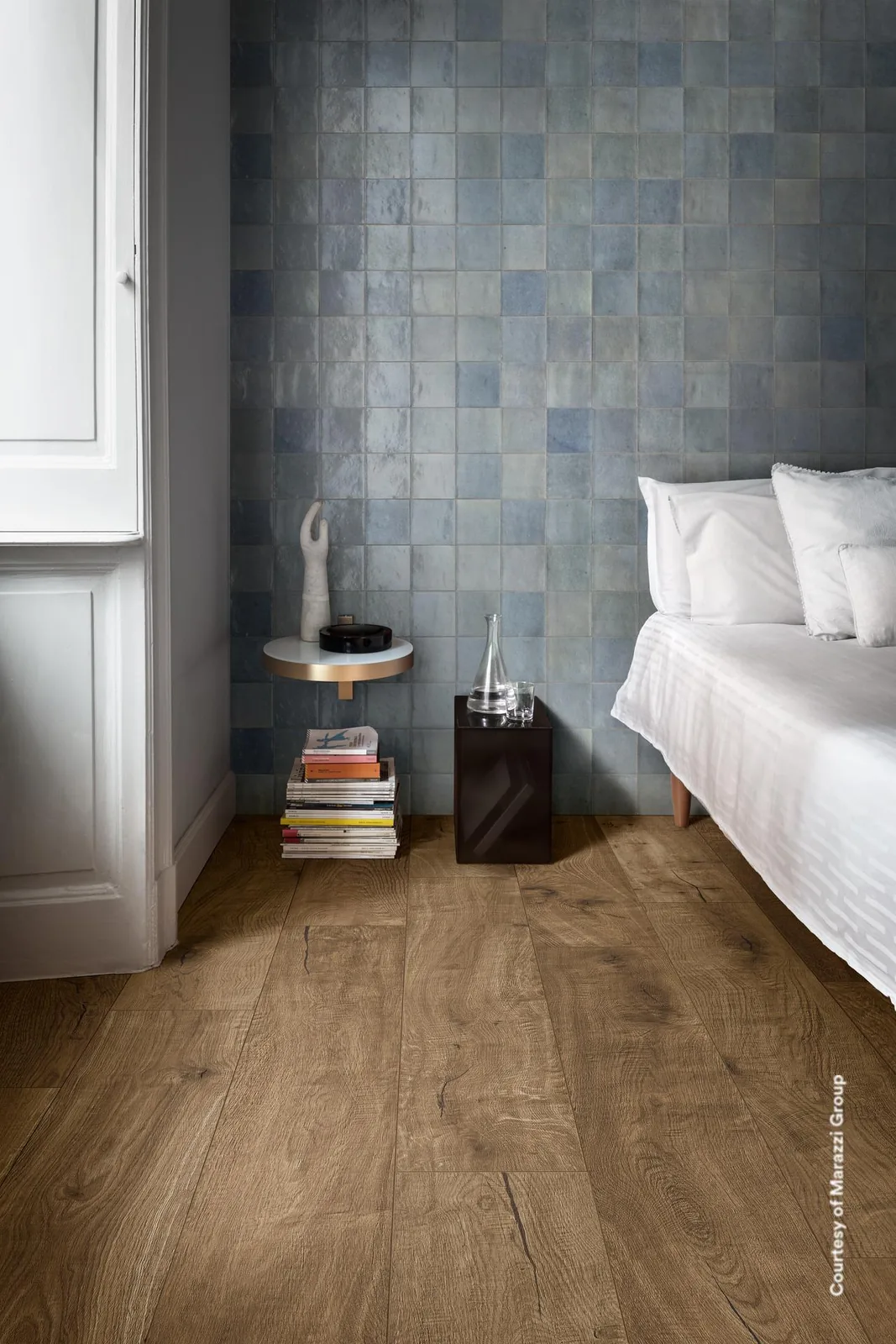 Schlafzimmer mit Wand aus Marazzi Zellige Cielo 10x10 cm in hellem Graublau hinter dem Bett, Holzboden