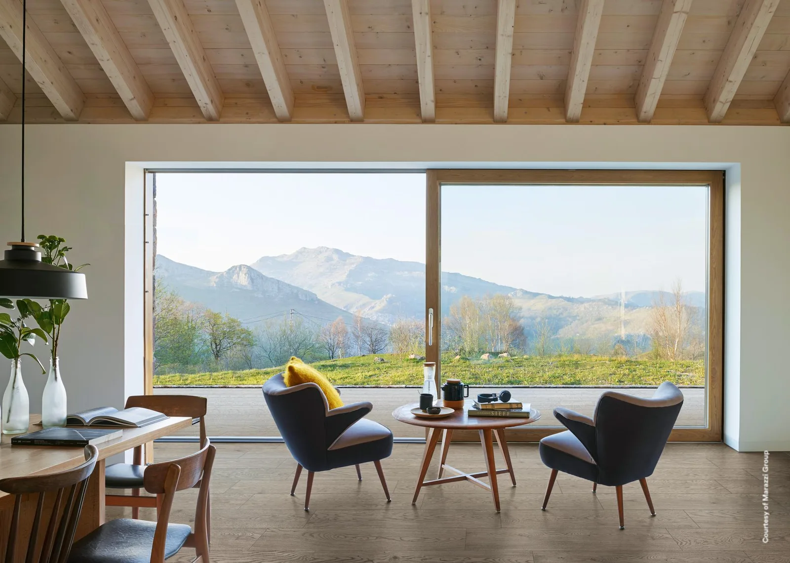 Wohn-Essraum mit Panoramafenster und Bergblick, Boden durchgehend in mittelbraunen Holzoptik-Planken verlegt.
