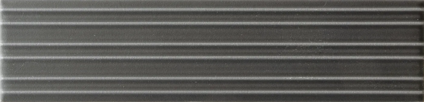 Rechteckige Wandfliese in dunklem Anthrazitgrau, matt, mit parallelem Rillenrelief, im Format 6x24,6 cm.