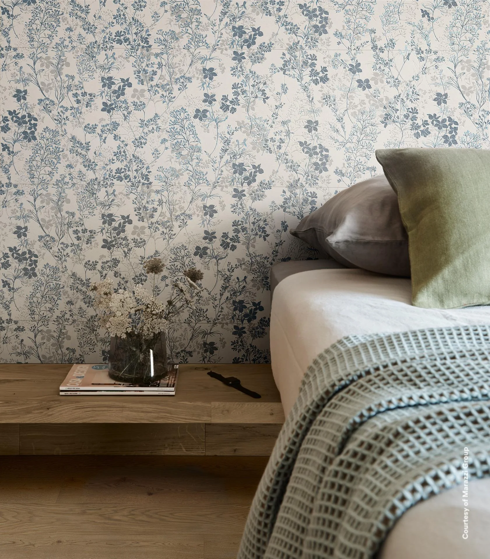 Bettkopfende vor hell gefliester Wand mit blauem Blumenmuster, Holzbank mit Büchern und grüner Strickdecke