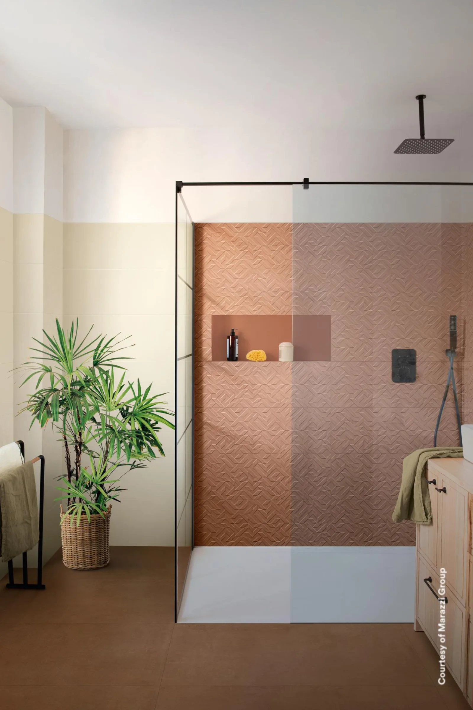 Dusche mit Glaswand, terrakottafarbener Reliefwand und Zimmerpflanze auf terrakottabraunem Betonoptik-Boden.