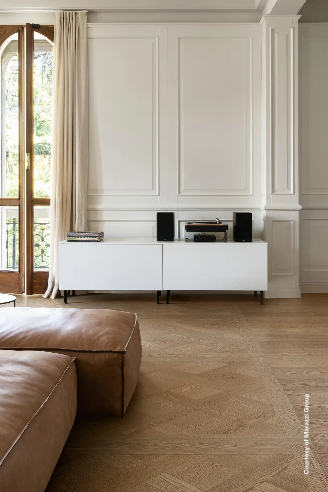 Wohnraum mit weißem Sideboard und braunem Ledersofa auf mittelbraunem Kassettenparkett in Holzoptik.
