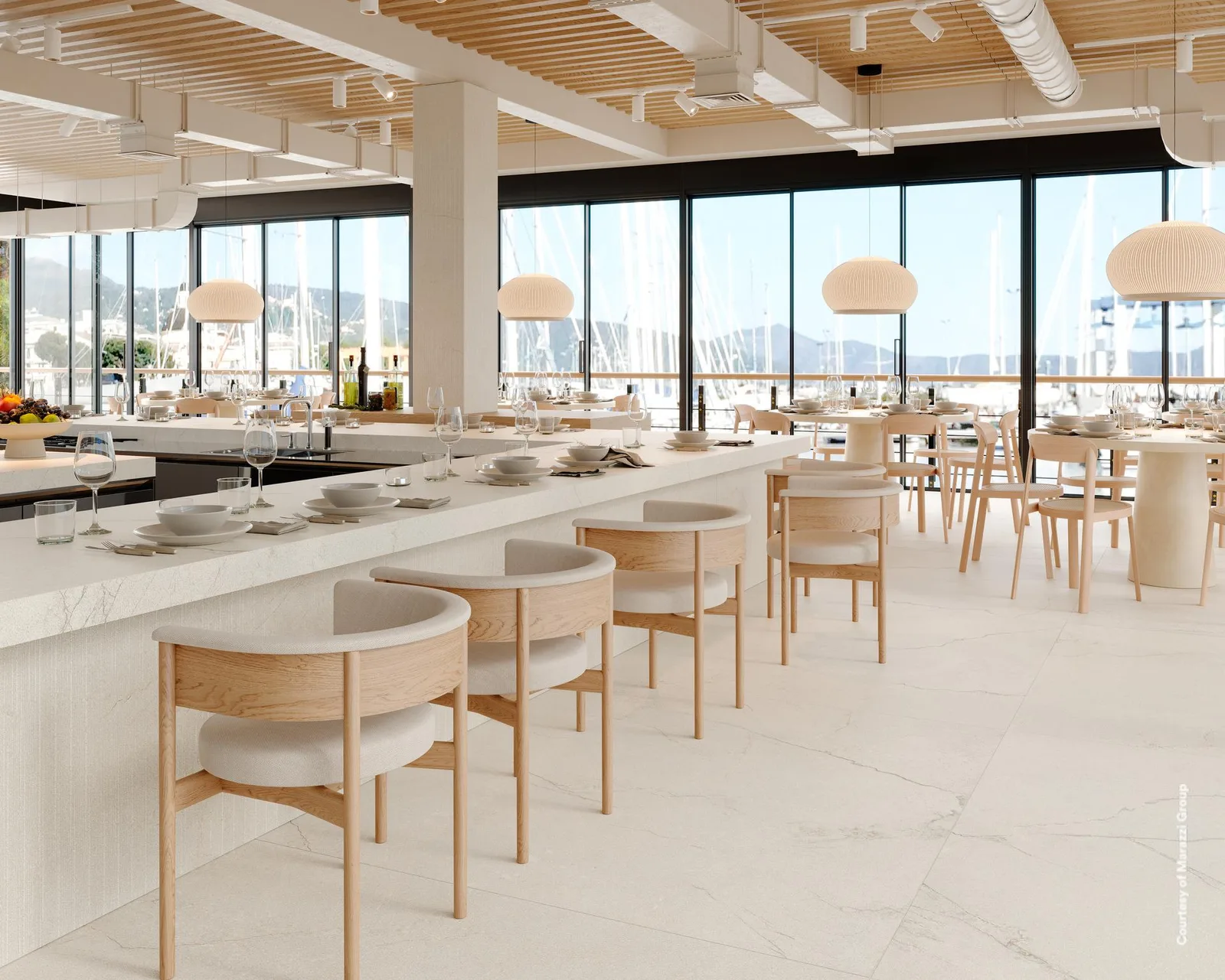 Restaurant mit Boden in weißer Steinoptik, Theke mit gerillter Front, Holzstühlen und Blick auf den Hafen.