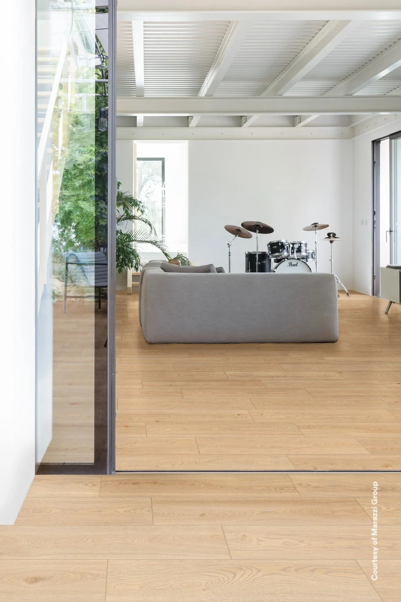 Blick durch eine Glasschiebetür auf graues Sofa und Schlagzeug, durchgehender Holzdielenboden