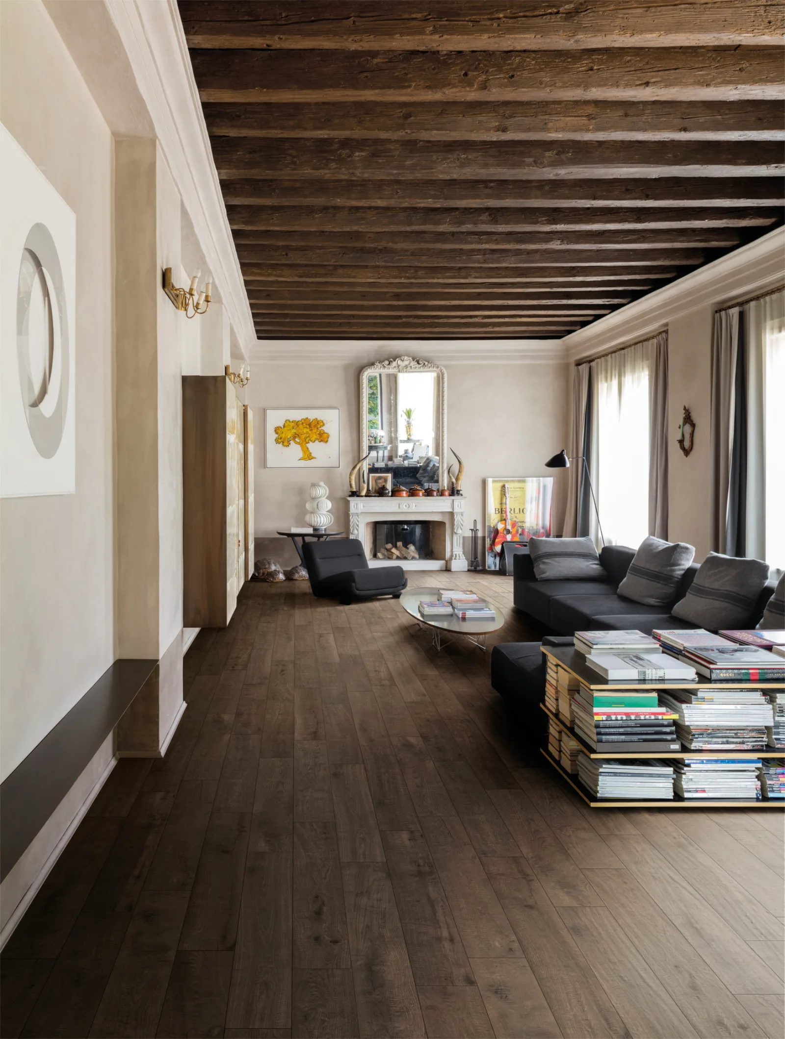 Wohnzimmer mit Holzbalkendecke, Kamin und dunklem Sofa auf Dielenboden in fast schwarzbrauner Holzoptik.