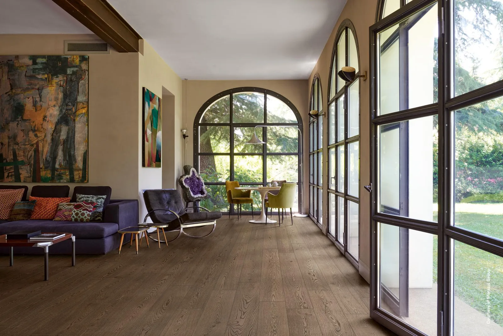 Wohnraum mit hohen Rundbogenfenstern und Sofa, Boden durchgehend in dunkelbraunen Holzoptik-Planken verlegt.