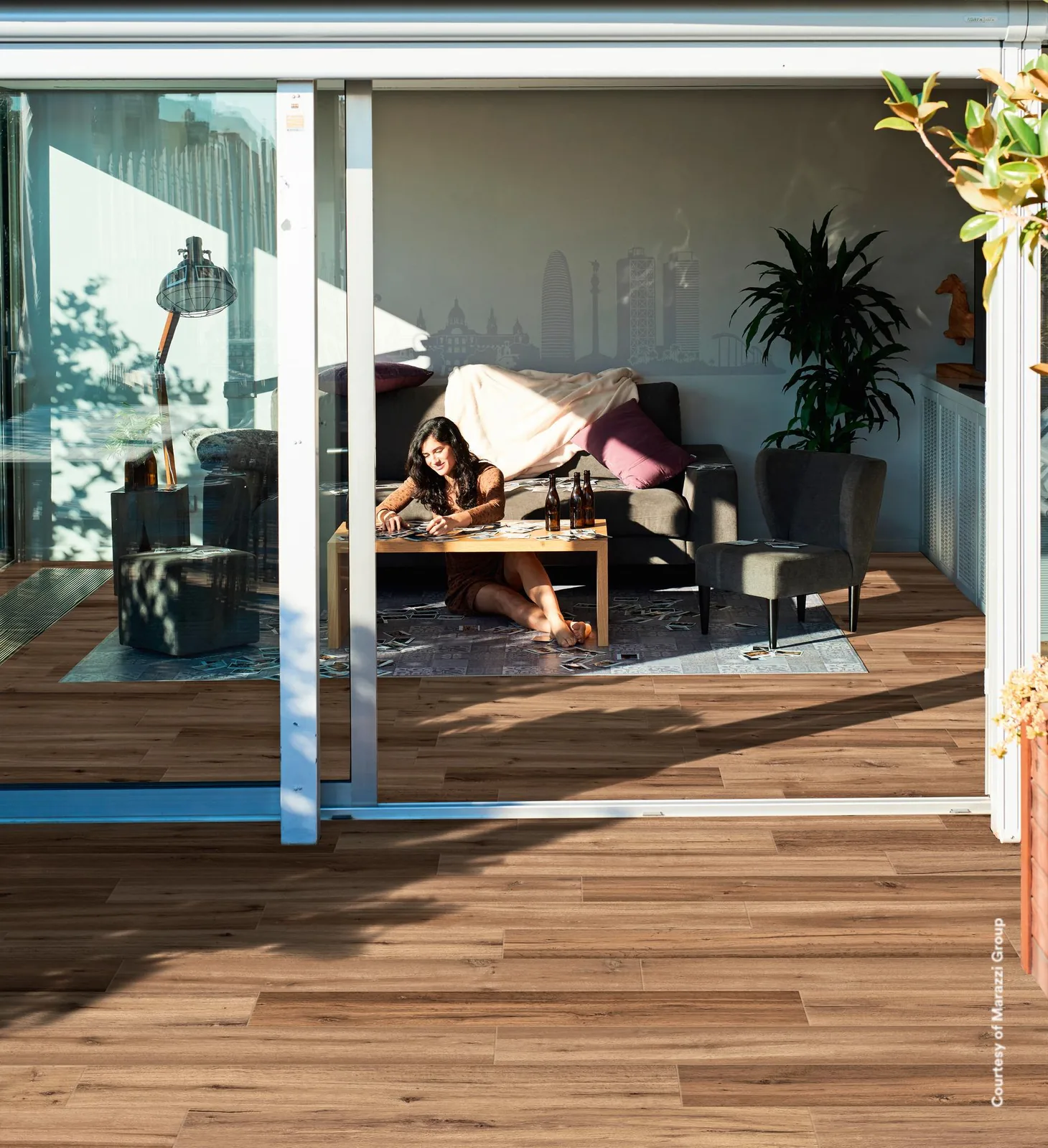 Wohnraum mit Sofa und Schiebetür zur Terrasse, innen und außen durchgehend mit braunen Holzoptik-Dielen belegt.