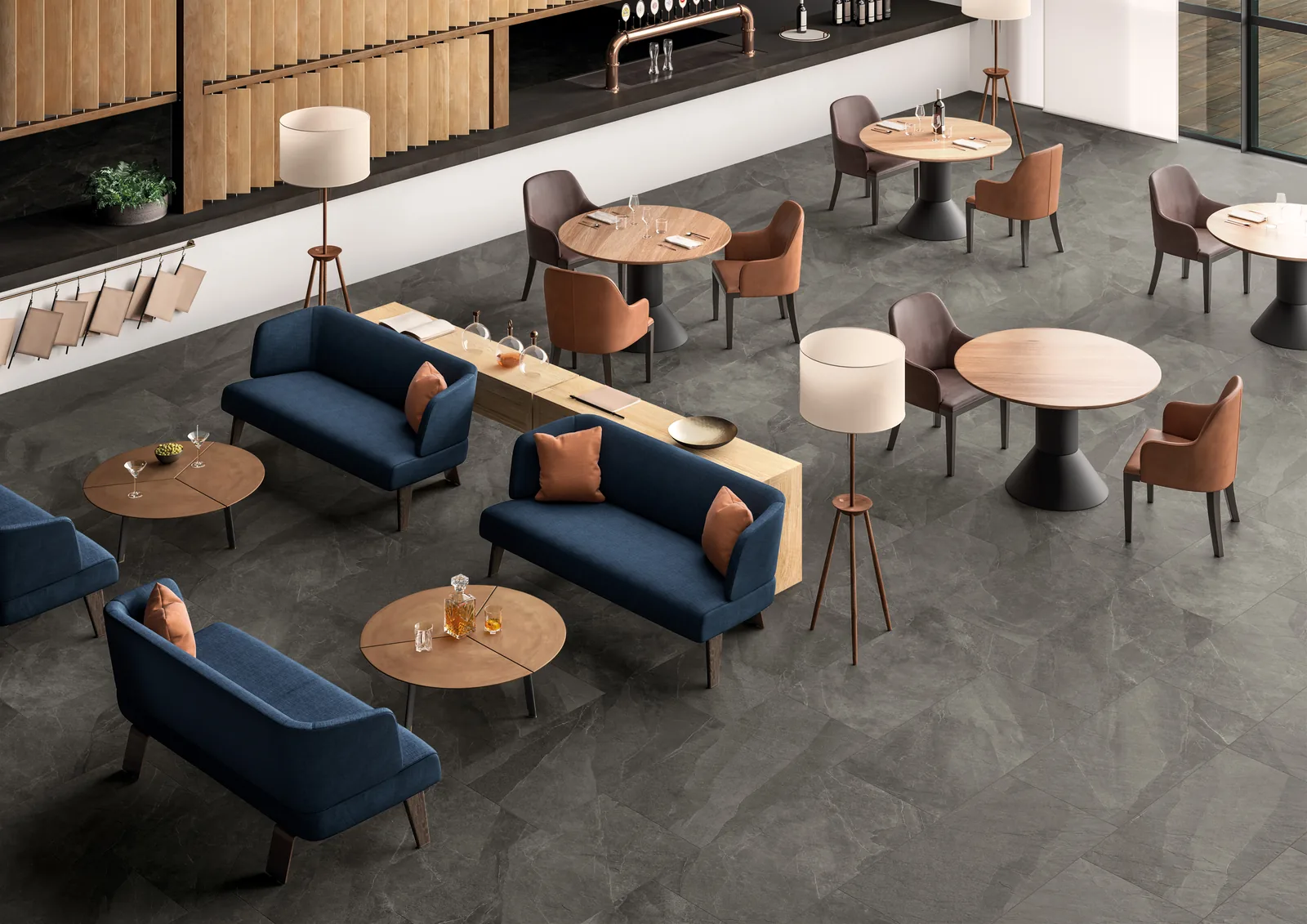 Café mit dunkelgrauem Boden in Schieferoptik aus verschiedenen Formaten, blauen Sofas und runden Holztischen