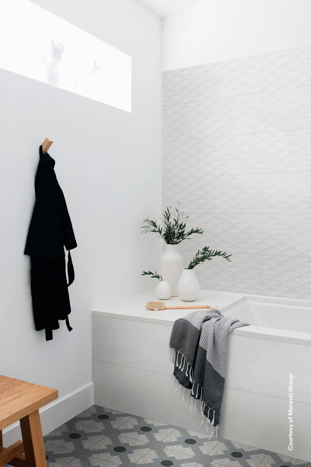 Helles Bad mit weißen Wandfliesen, rechts Rautenrelief über der Wanne, Bademantel am Haken