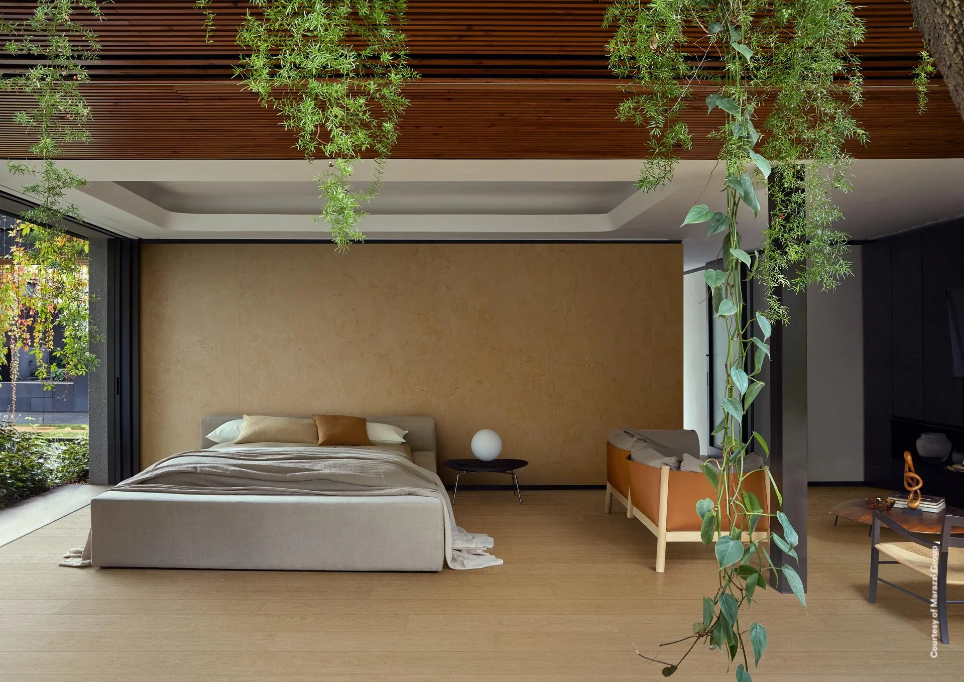 Schlafzimmer mit ockerfarbener Wand, Bett und Hängepflanzen auf hellen Holzoptik-Dielen zum Garten hin.