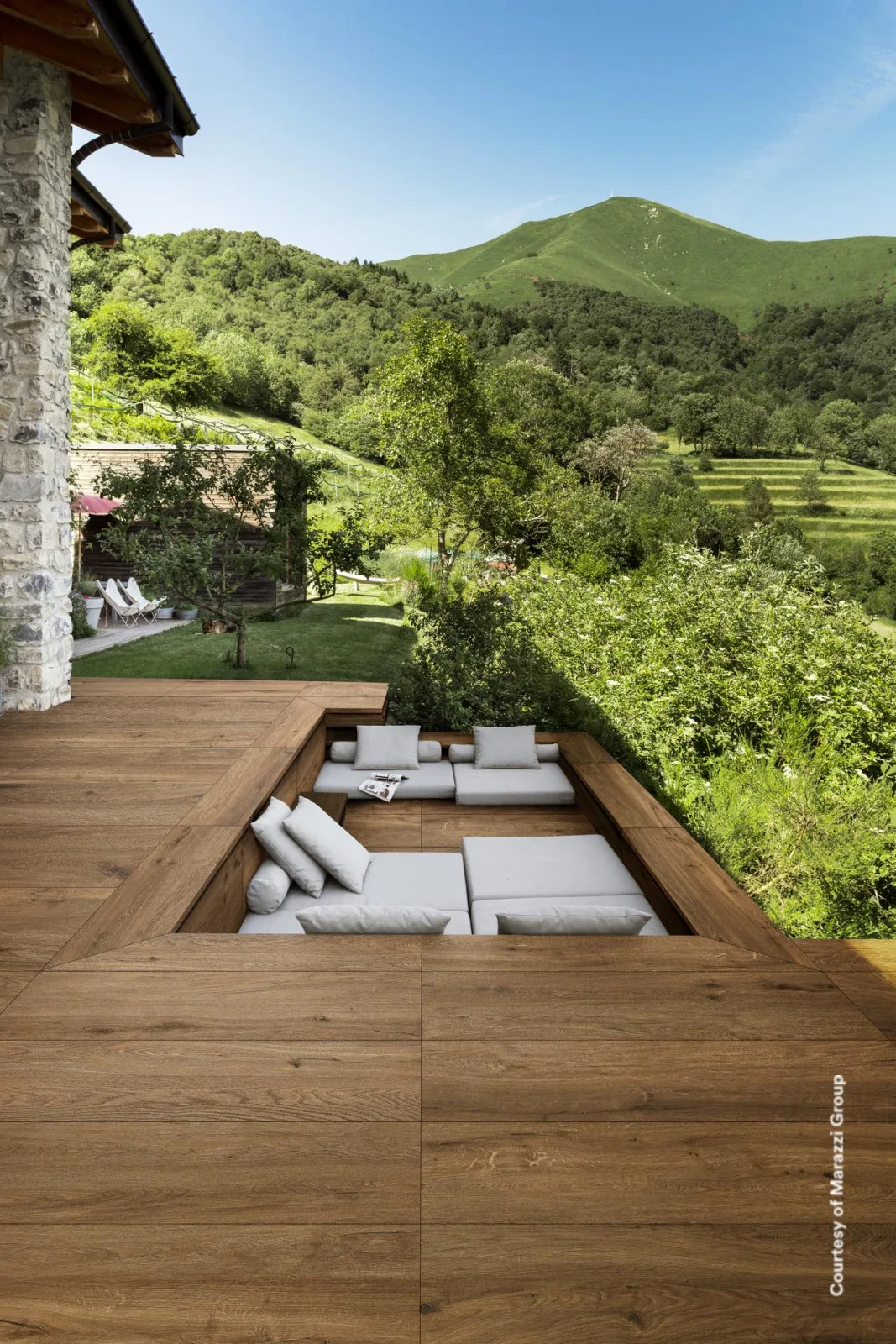 Marazzi Vero20 Castagno auf einer Bergterrasse: dunkelbraune Holzoptik-Dielen um eine versenkte Sitzecke mit Kissen