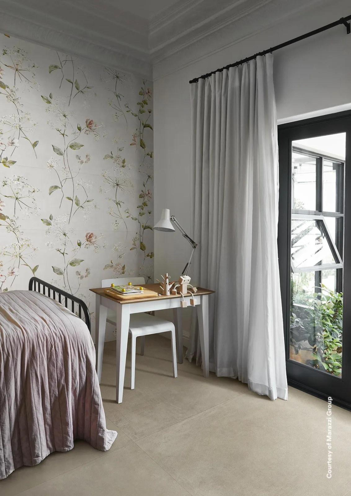 Schlafzimmer mit Bett, Schreibtisch und Fenster, die Wand dahinter mit zarten Blütenranken auf weißem Grund belegt.