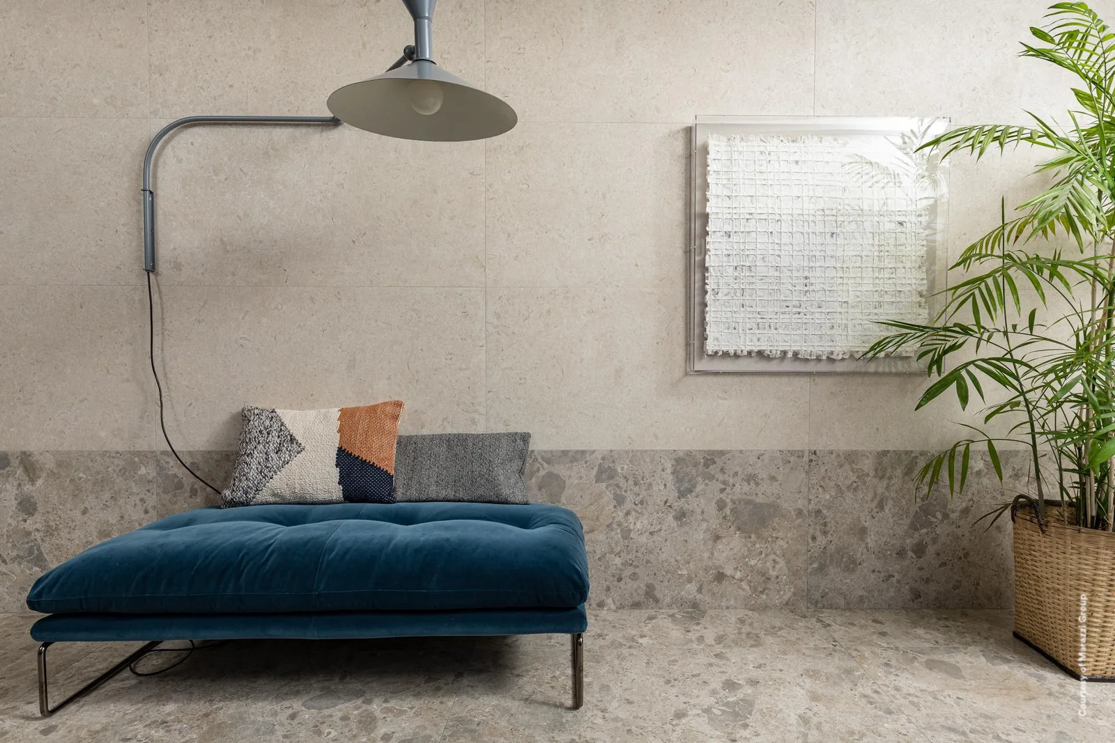 Wohnraum mit blauer Polsterliege und Bogenleuchte, Wand in sandbeiger Steinoptik, Sockel und Boden in Terrazzo-Optik.