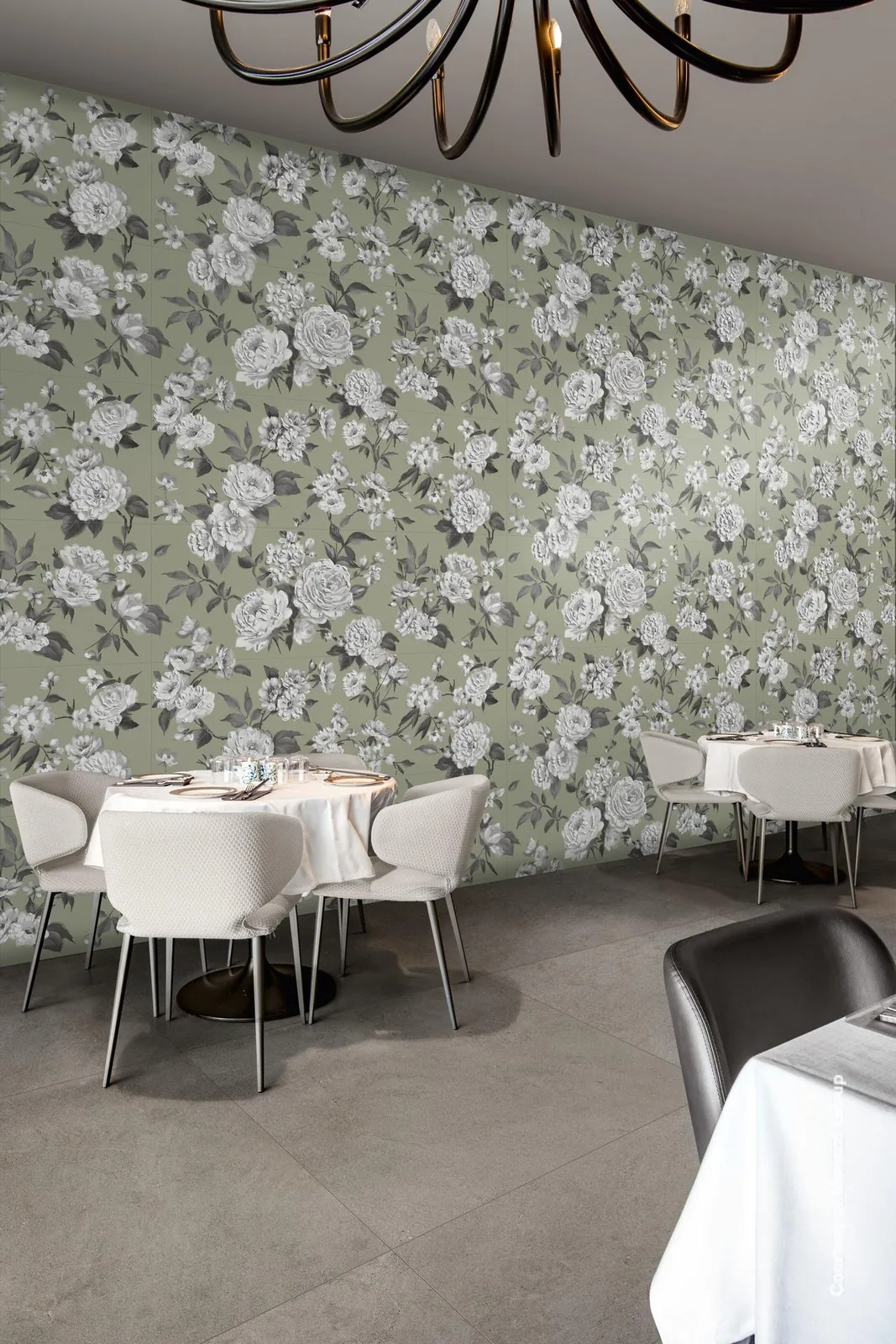 Restaurant mit gedeckten Tischen und Kronleuchter vor einer großen Wand mit grauen Rosen auf salbeigrünem Grund.