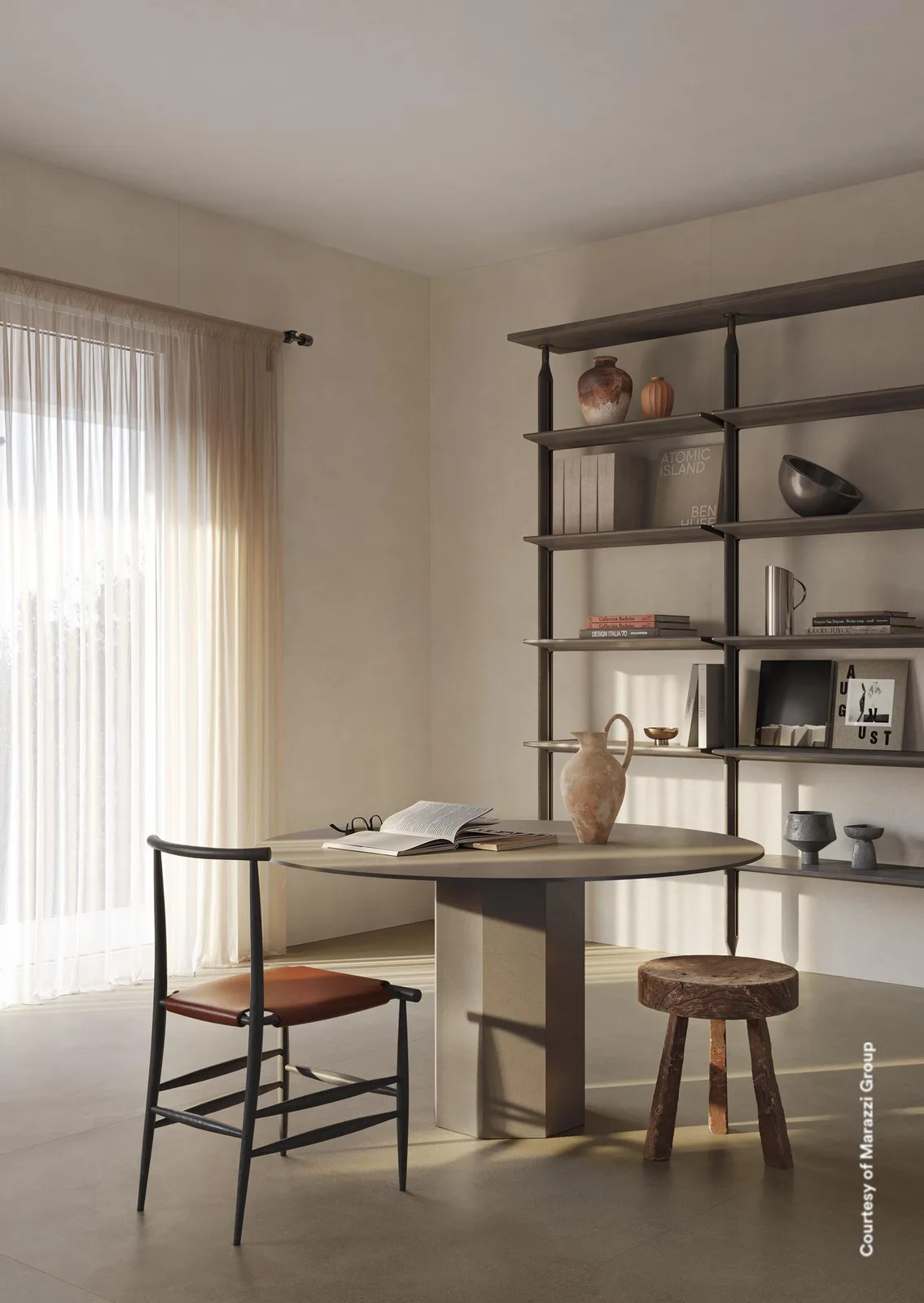 Arbeitsecke mit rundem Tisch, Holzhocker und schwarzem Regal auf taupefarbenem Boden vor heller Sandwand.