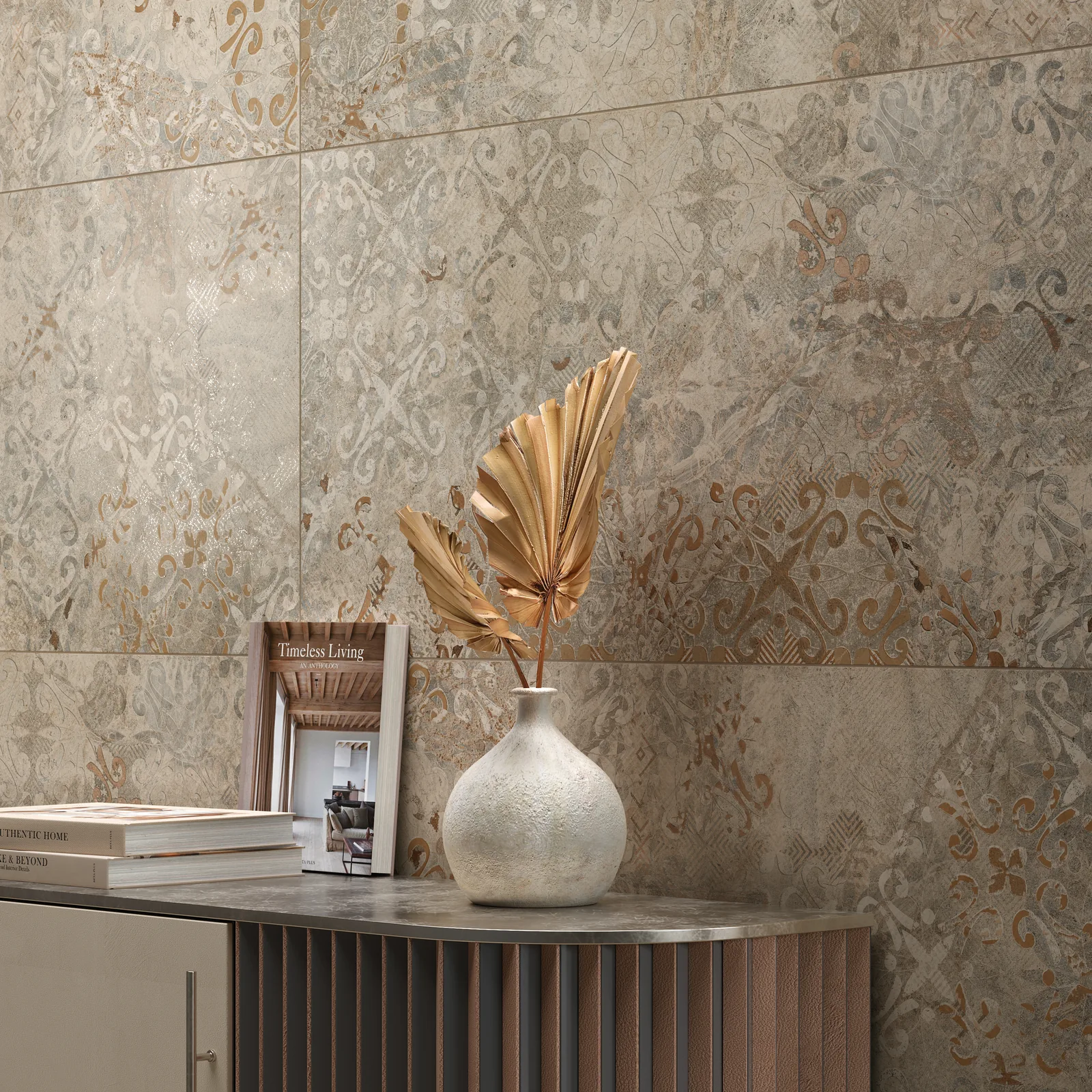 Wand aus beigegrauen Dekorfliesen mit verblasstem Ornament-Patchwork, davor ein Sideboard mit Vase und Bildband.