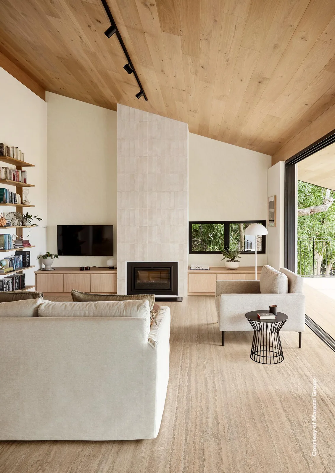 Wohnraum mit Boden in beiger Travertin-Optik, Holzdecke, Kamin und großem weißem Sofa.