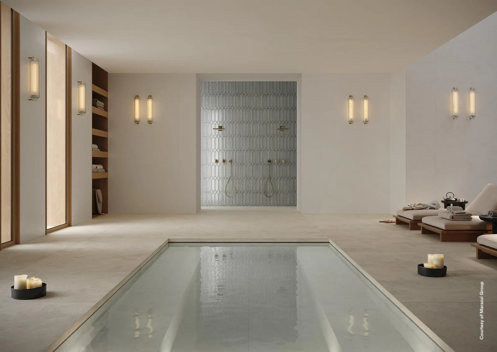 Innenpool mit Wandleuchten und Mosaikwand, Boden und Wände aus großen Platten in hellem, fast weißem Ton.