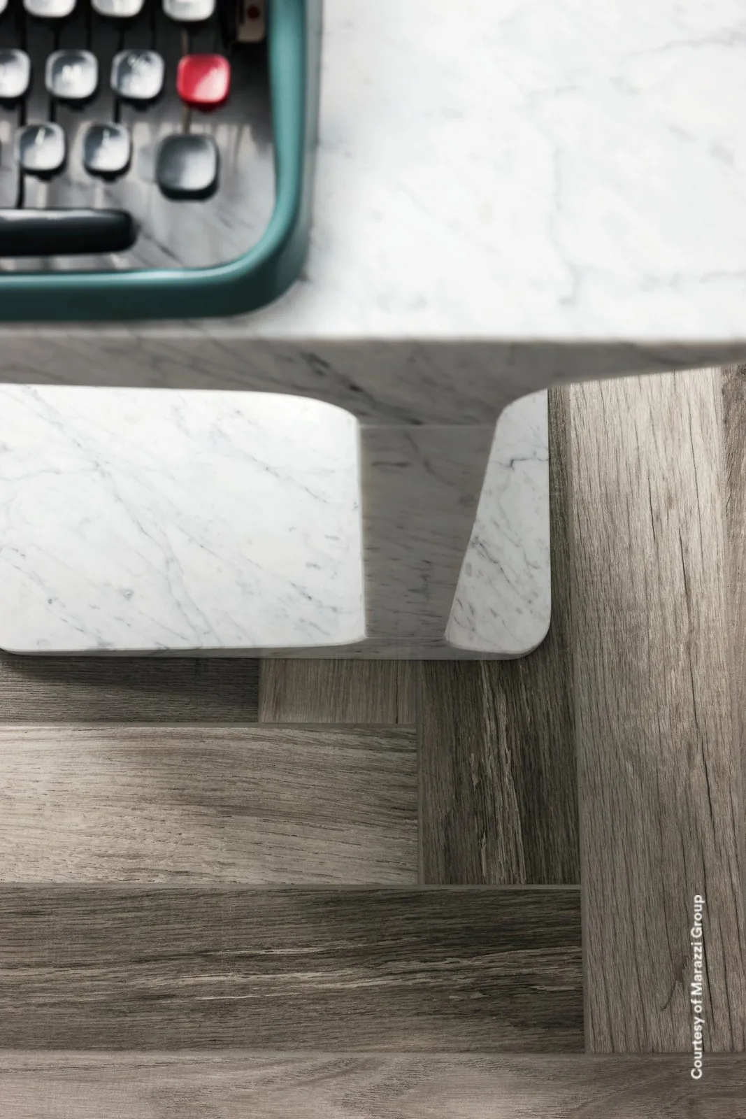 Graue Holzoptik-Fliese Treverkfusion Grey als Fischgrätboden unter einem Tisch mit Marmorplatte