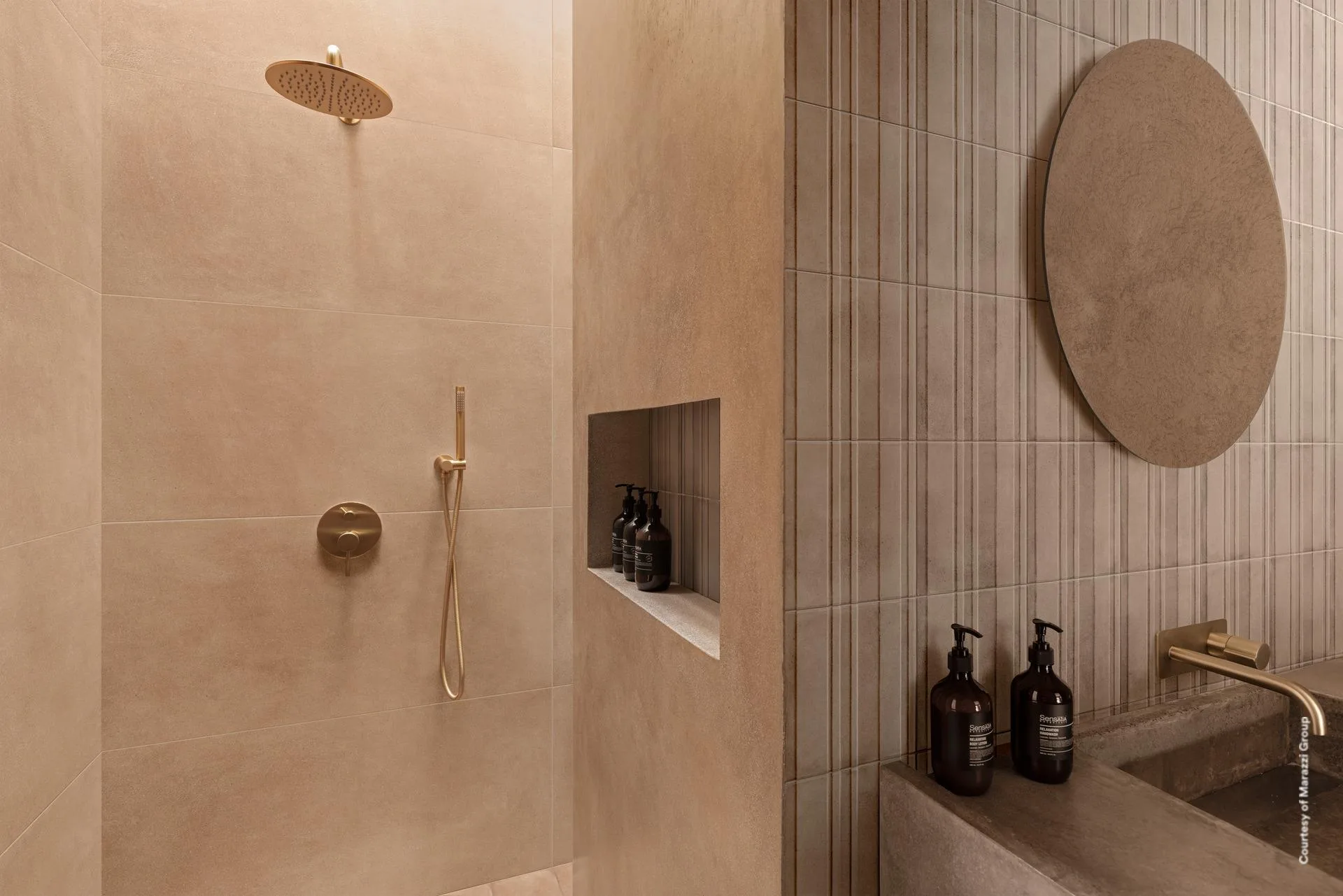 Dusche mit goldener Armatur, Wandnische und Rundspiegel, warm beigebraune Großformatfliese an der Rückwand.