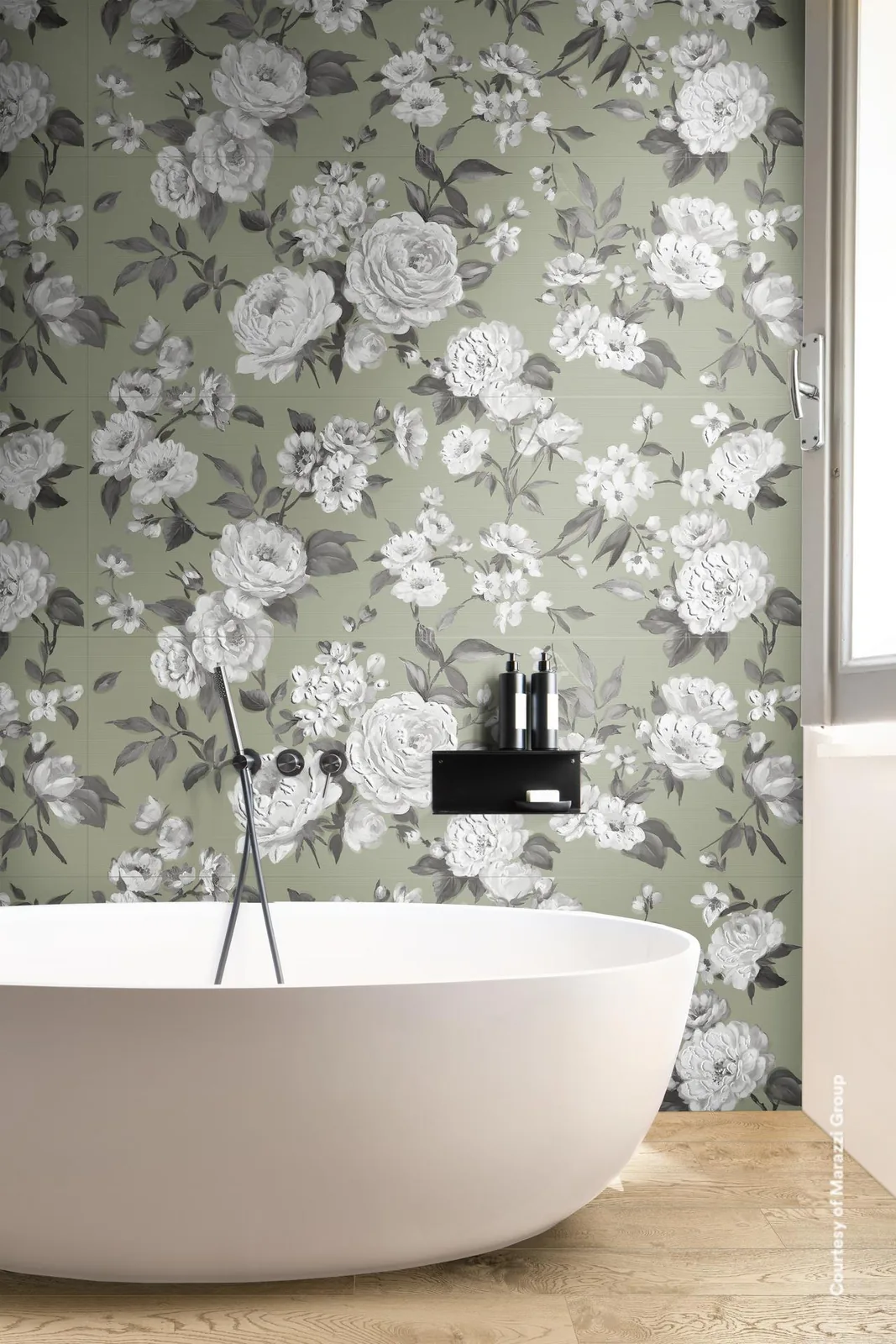 Freistehende Badewanne vor einer Wand mit grauen und weißen Rosen auf salbeigrünem Grund, Armatur an der Wand.