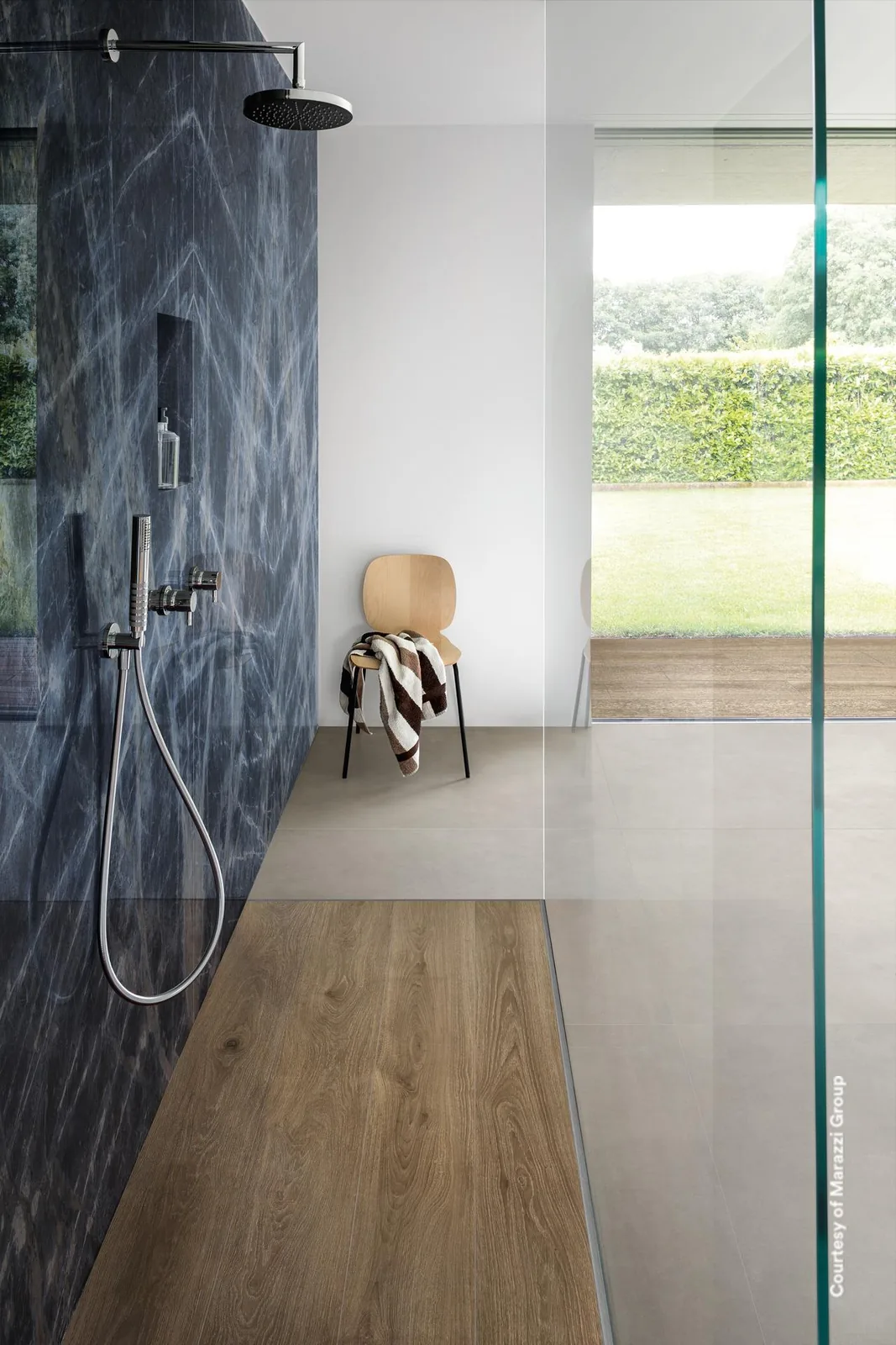 Dusche mit Wand in tiefblauer Marmoroptik mit weißen Adern, Holzboden im Duschbereich und Blick in den Garten.