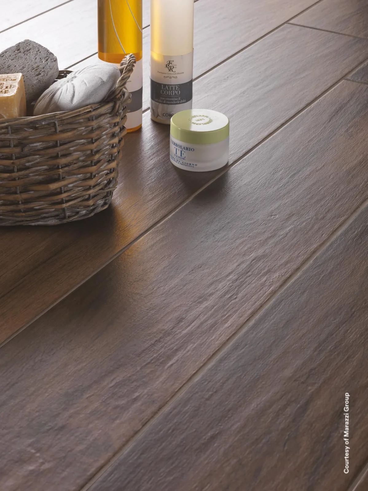 Weidenkorb mit Handtuch und Kosmetikflaschen auf dunkelbraunen Holzoptik-Dielen mit feiner Maserung.