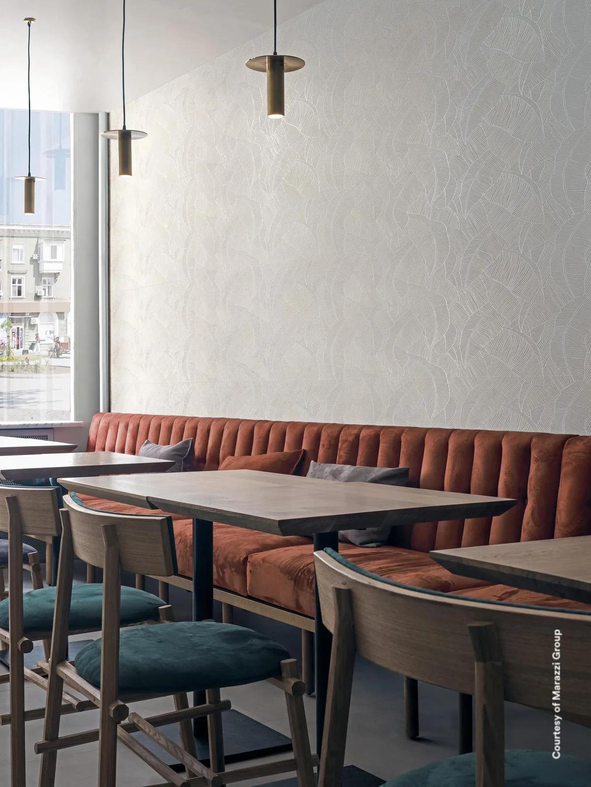 Restaurant mit roter Sitzbank, Holztischen und Pendelleuchten vor einer hellen Wand mit feinem Blattrelief.