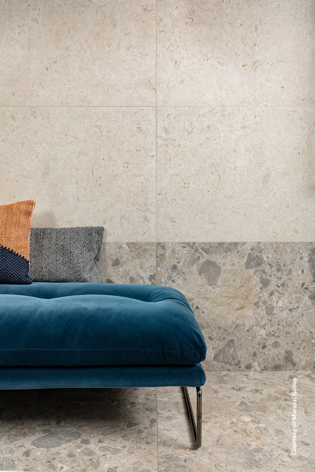 Wohnraum mit blauer Polsterliege, Wand in sandbeiger Steinoptik, unterer Wandbereich und Boden in Terrazzo-Optik.