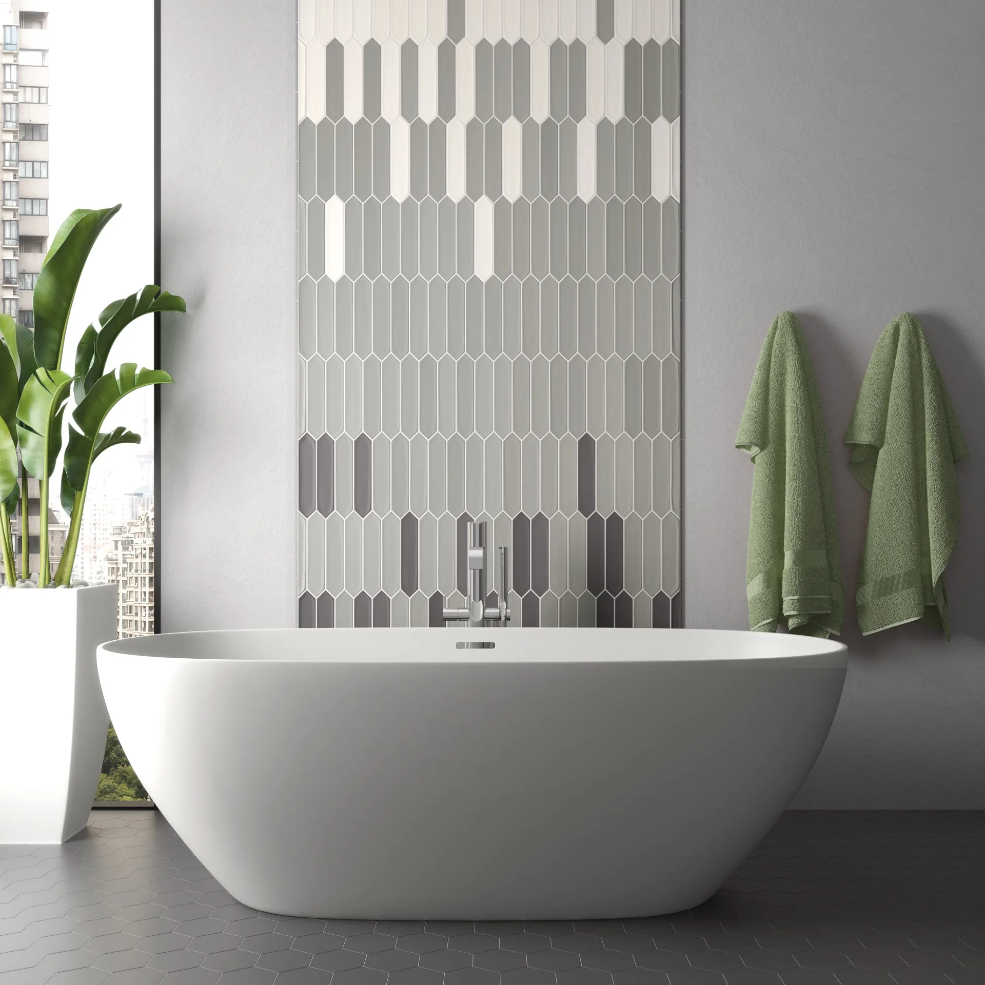 Bad mit hellgrauen, spitz zulaufenden Wandfliesen hinter freistehender Badewanne und grünen Handtüchern.