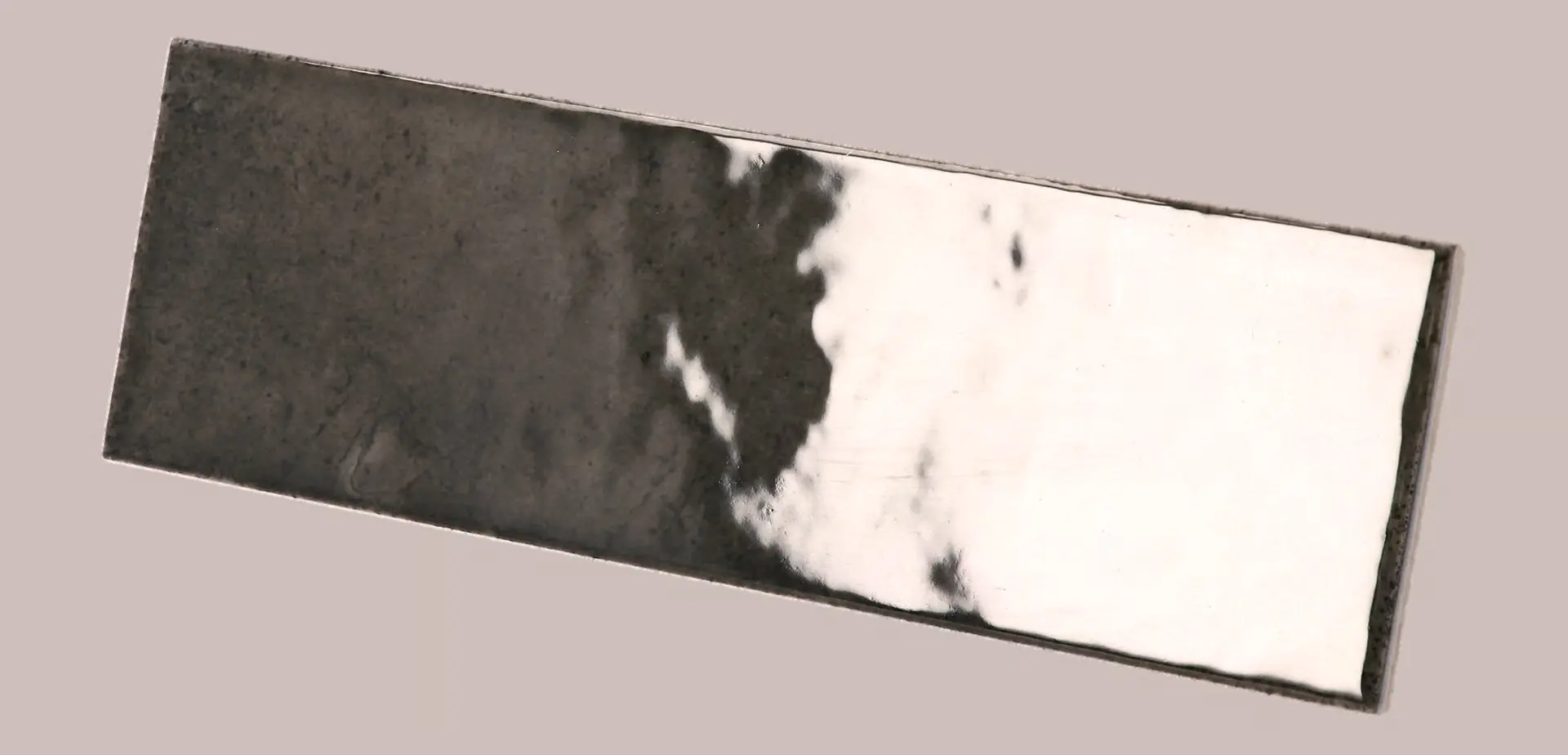 Hanoi Wandfliese in Black Ash Glasur, Format 6,5x20 cm, schräge Studio Aufnahme mit sichtbarem Glasurglanz.