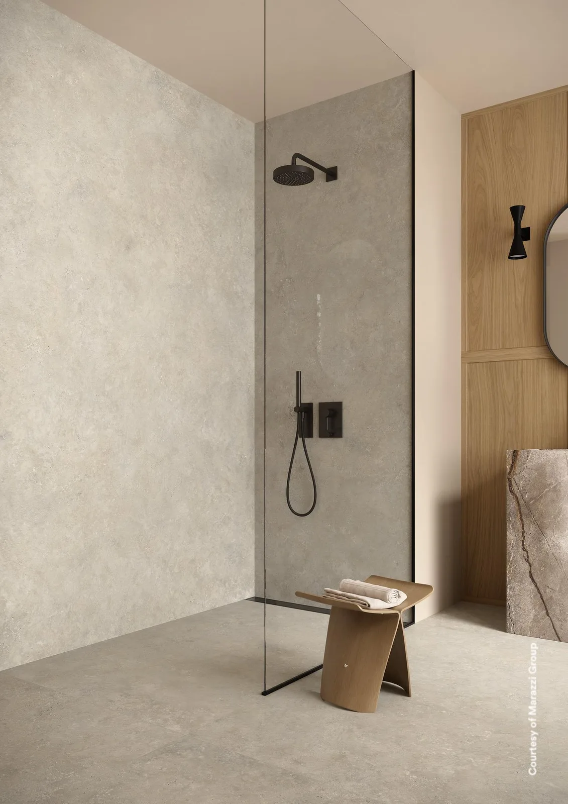 Walk-in-Dusche mit Wänden und Boden in graubeiger Steinoptik, schwarzer Armatur und Holzhocker.