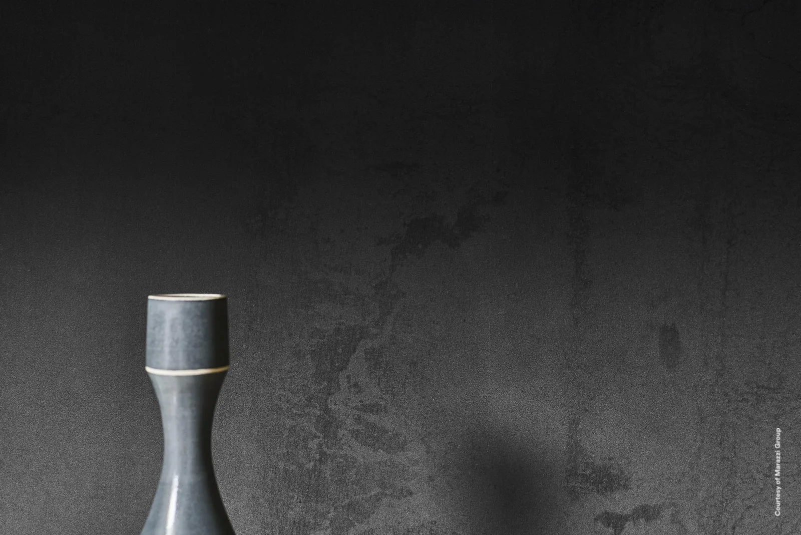 Wand mit Marazzi Grande Metal Look Iron Dark in Metalloptik, dunkle Patina-Struktur, davor eine blaue Vase