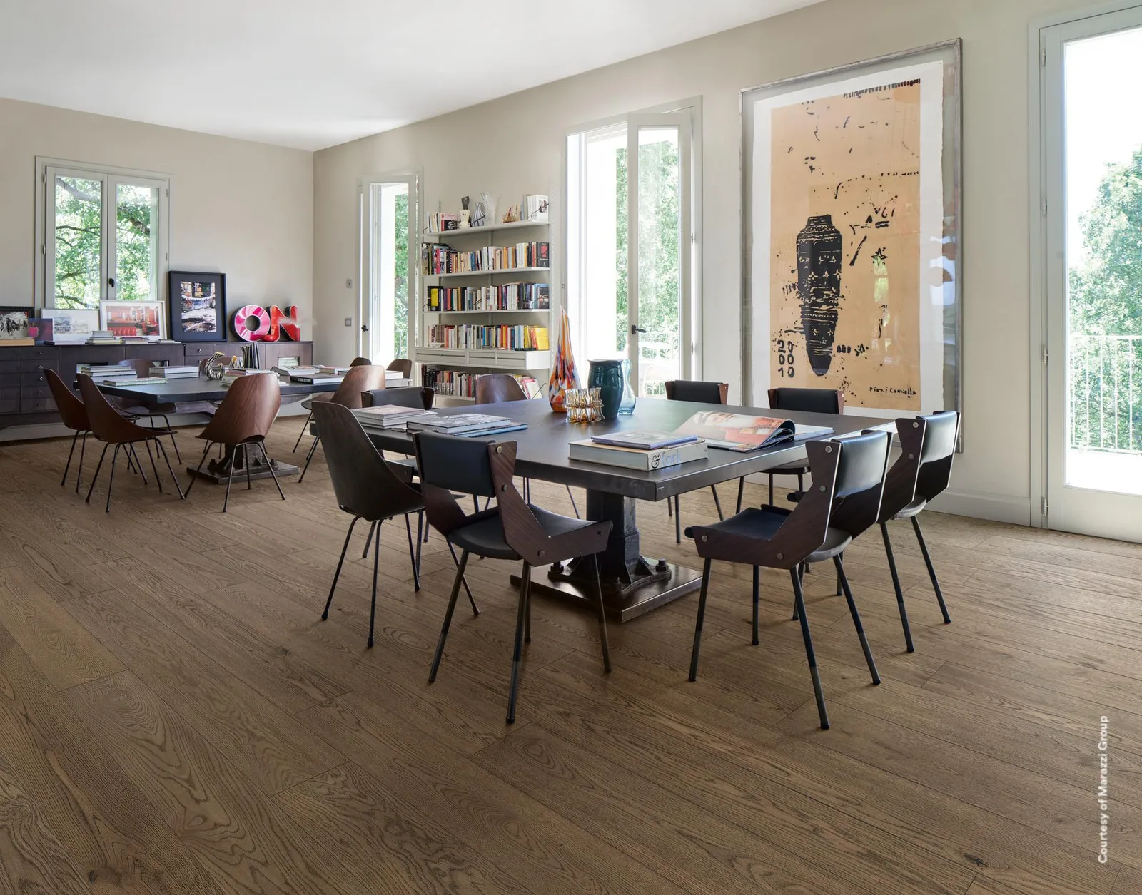 Großer Essraum mit langem Tisch, Stühlen und Bücherwand, Boden in dunkelbraunen Holzoptik-Planken verlegt.
