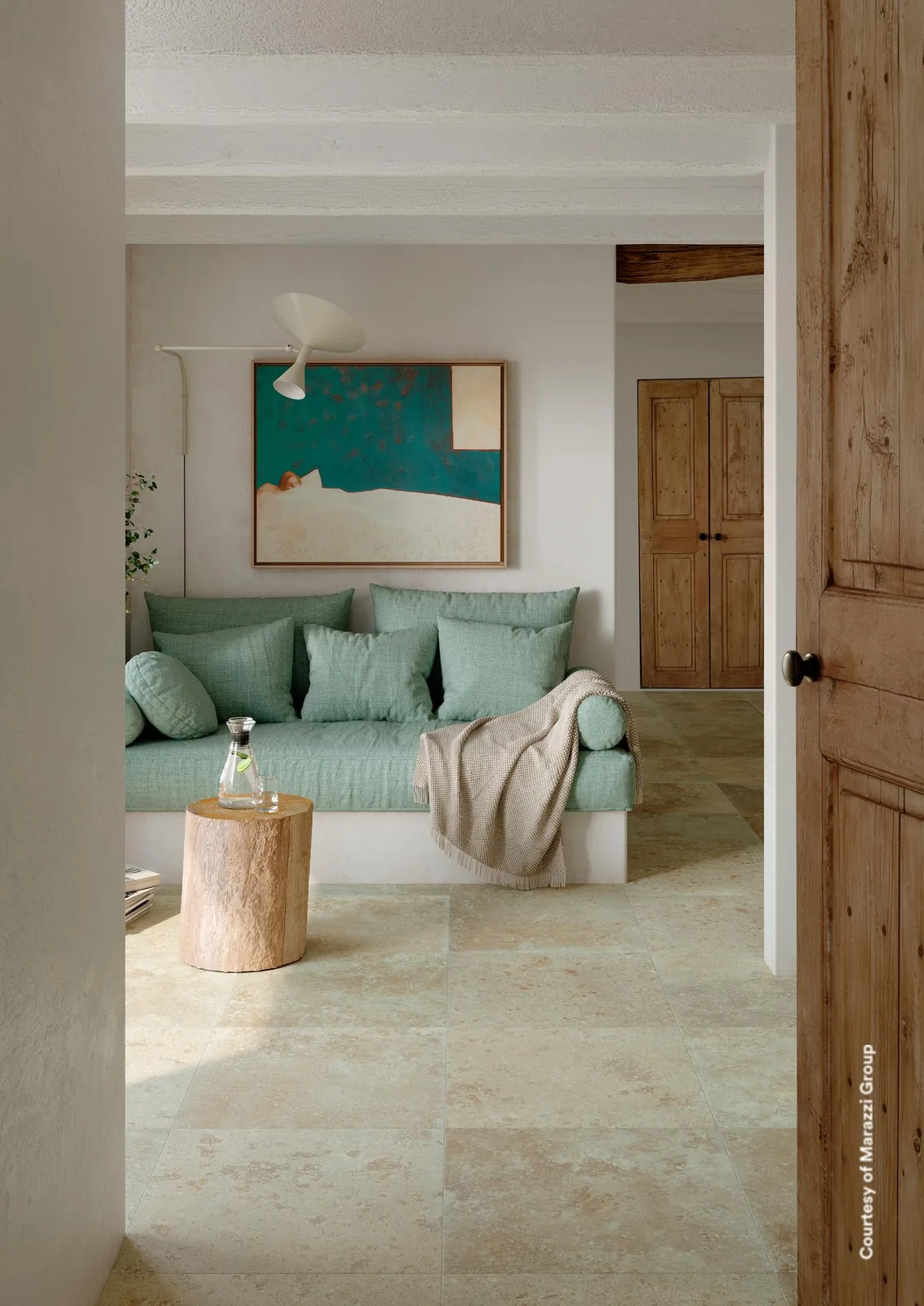 Wohnraum mit hellbeigen Steinoptik-Bodenfliesen, Sofa mit türkisen Kissen und Blick durch eine offene Holztür
