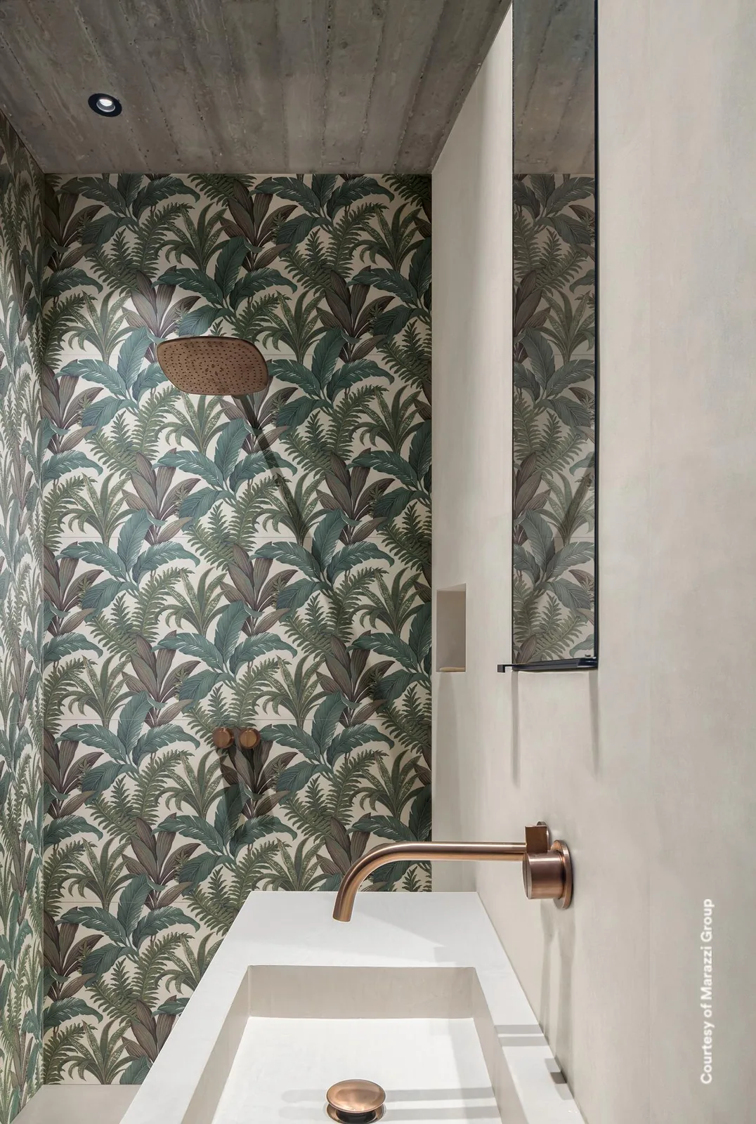 Dusche mit großflächigem Palmblatt-Dekor an der Wand, daneben eine cremeweiße Betonoptik-Wand und ein weißes Waschbecken.