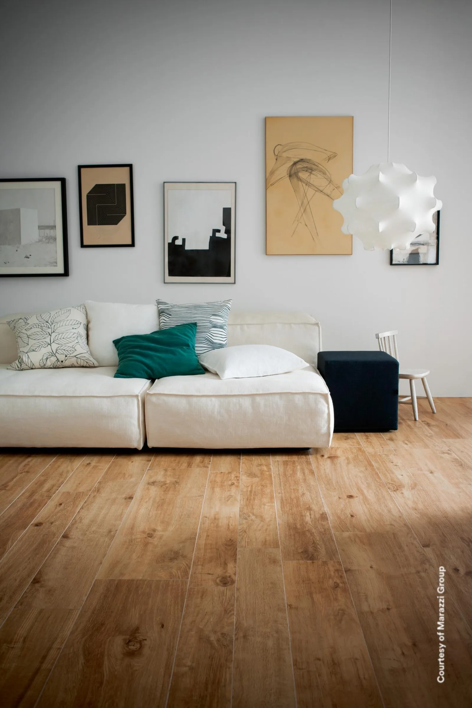 Wohnzimmer mit honigfarbenem Dielenboden in Holzoptik, weißem Sofa mit grünem Kissen, Bildern und Hängeleuchte.