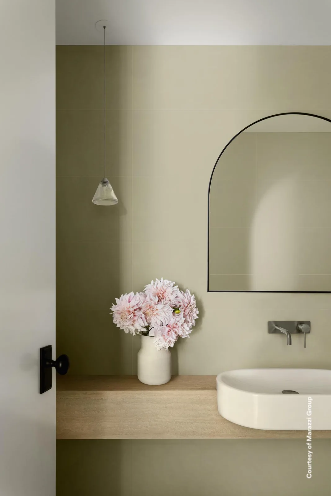 Gäste-WC mit salbeigrünen matten Wandfliesen, rundem Aufsatzbecken auf Holzablage und Spiegel mit Rundbogen.