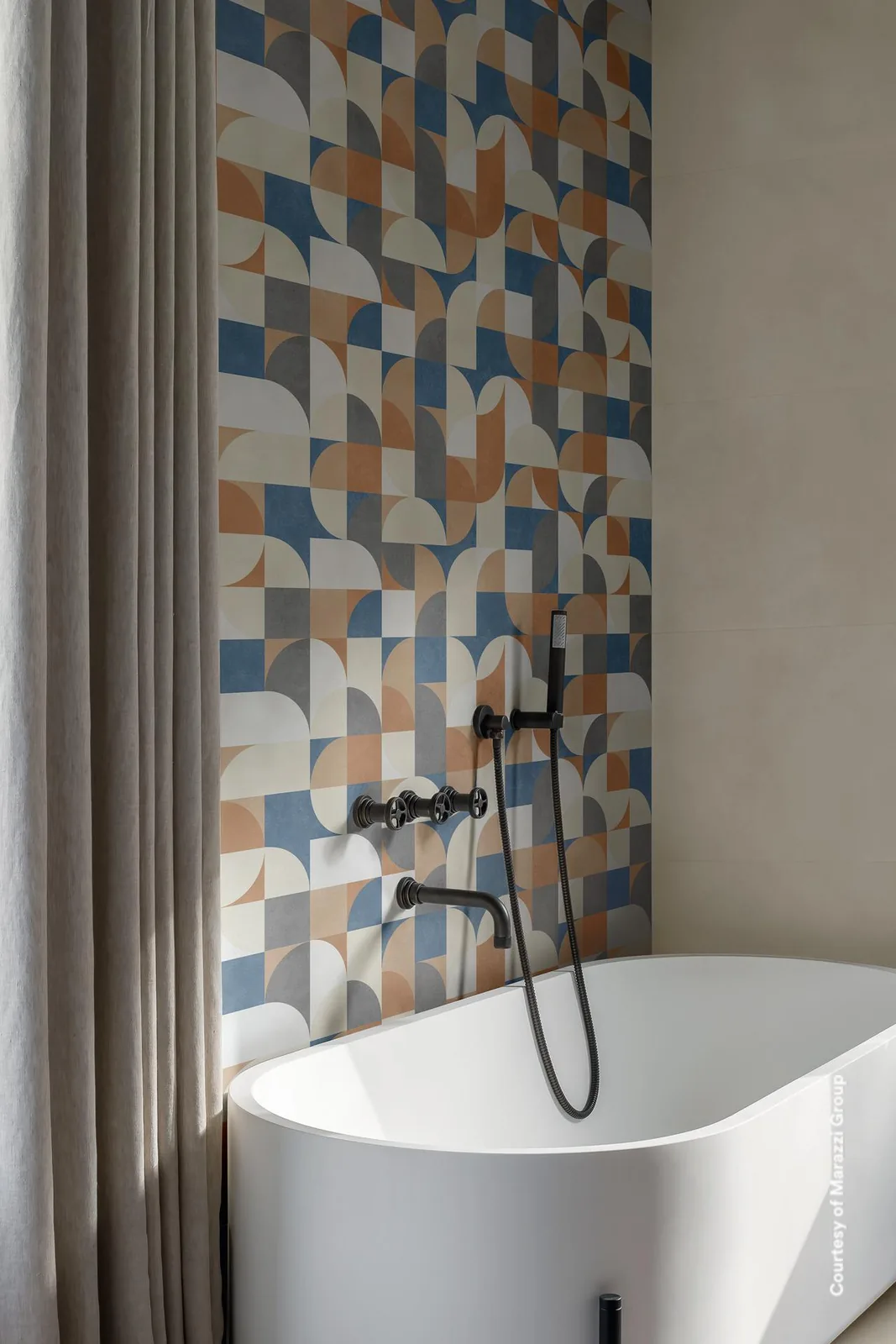 Bad mit geometrischem Dekor aus Viertelkreisen in Blau, Rostbraun und Grau hinter der Wanne, umgeben von heller Beigewand.
