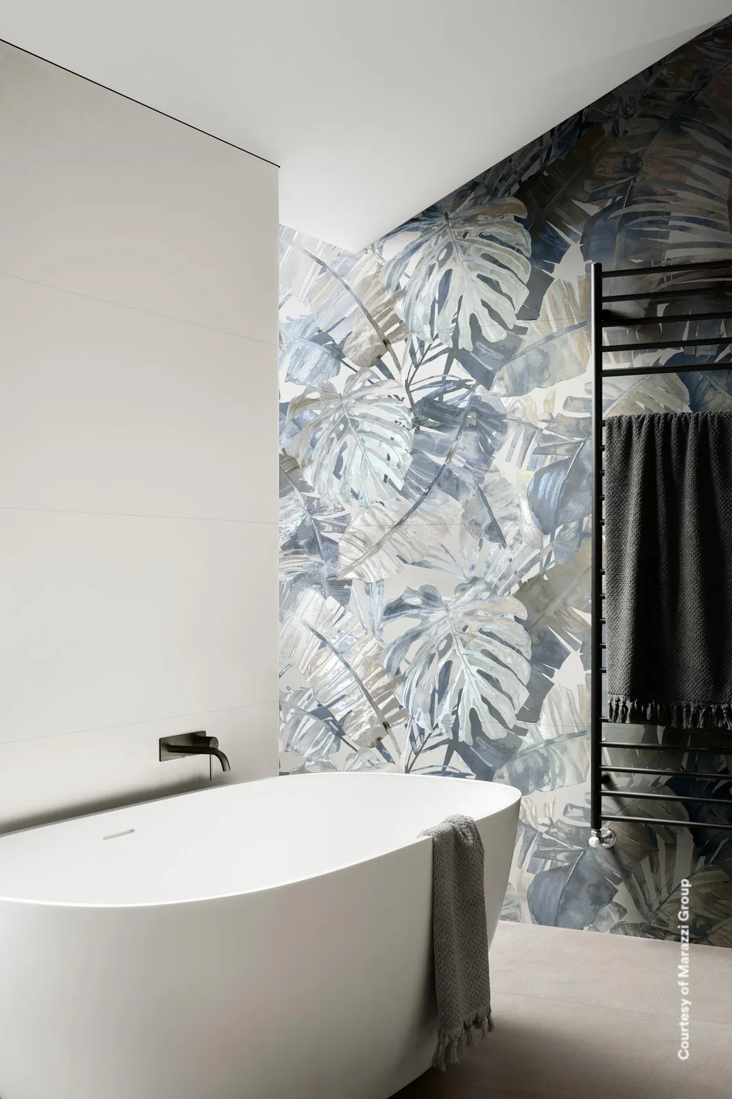 Bad mit freistehender Wanne und Handtuchheizkörper, eine Wand mit blaugrauen Tropenblättern, daneben glatte weiße Wand.