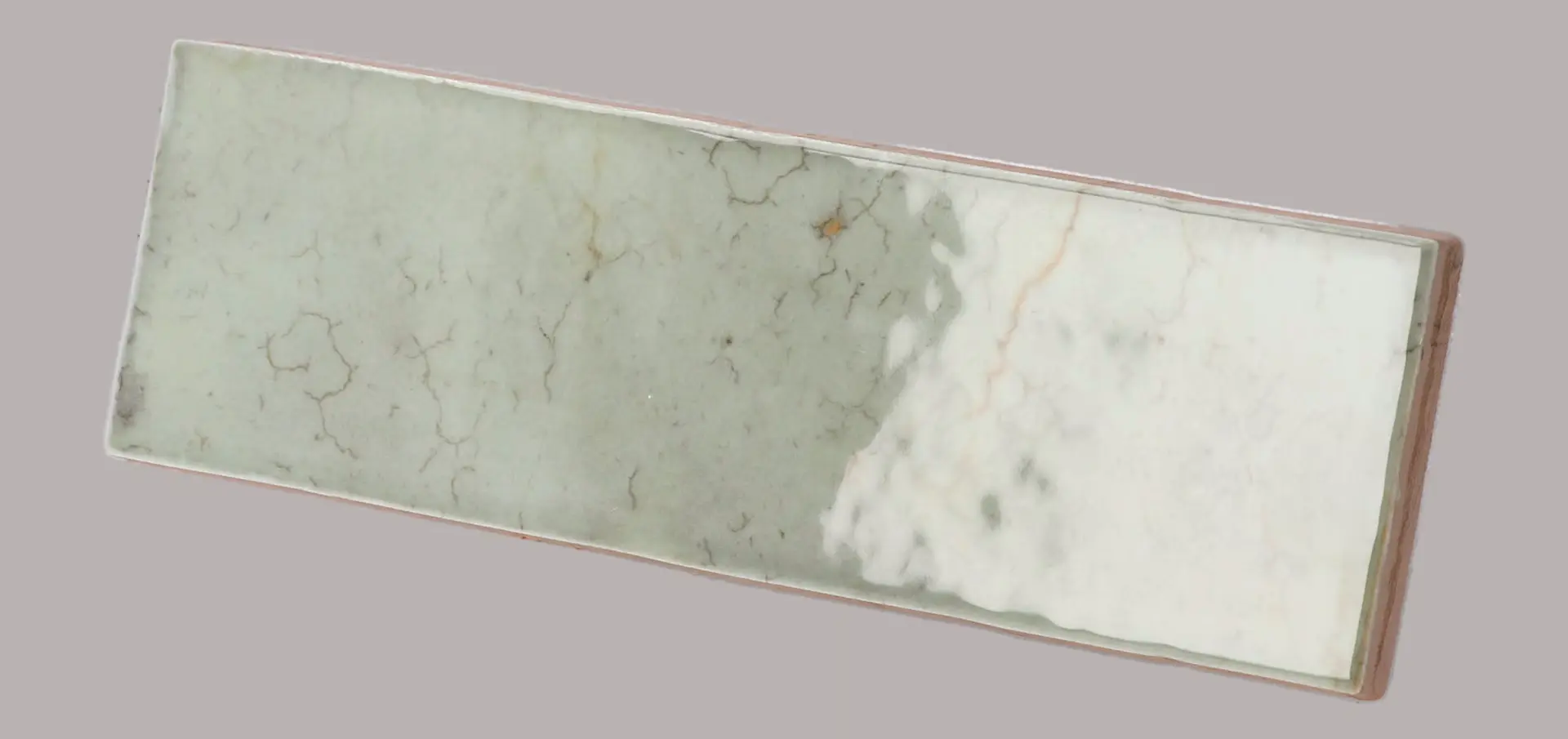 Hanoi Wandfliese in Celadon Glasur, Format 5,1x16,1 cm, schräge Studio Aufnahme mit sichtbarem Glasurglanz.