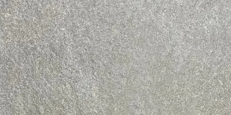 Nahaufnahme einer mittelgrauen Steinoberfläche mit feiner, leicht wolkiger Maserung in Grautönen.