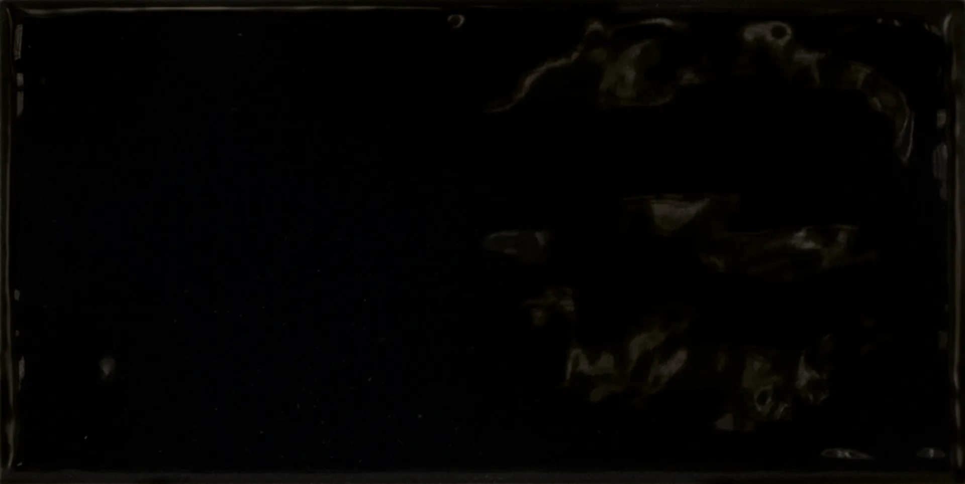 Einzelne schwarze Rechteckfliese mit matter Glasuroberfläche im Format 7,5×15 cm und sanften Lichtreflexen.