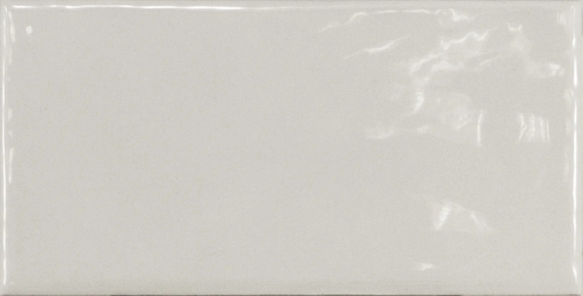 Einzelne hellgraue Rechteckfliese mit glänzender Glasuroberfläche im Format 7,5×15 cm und sanften Lichtreflexen.