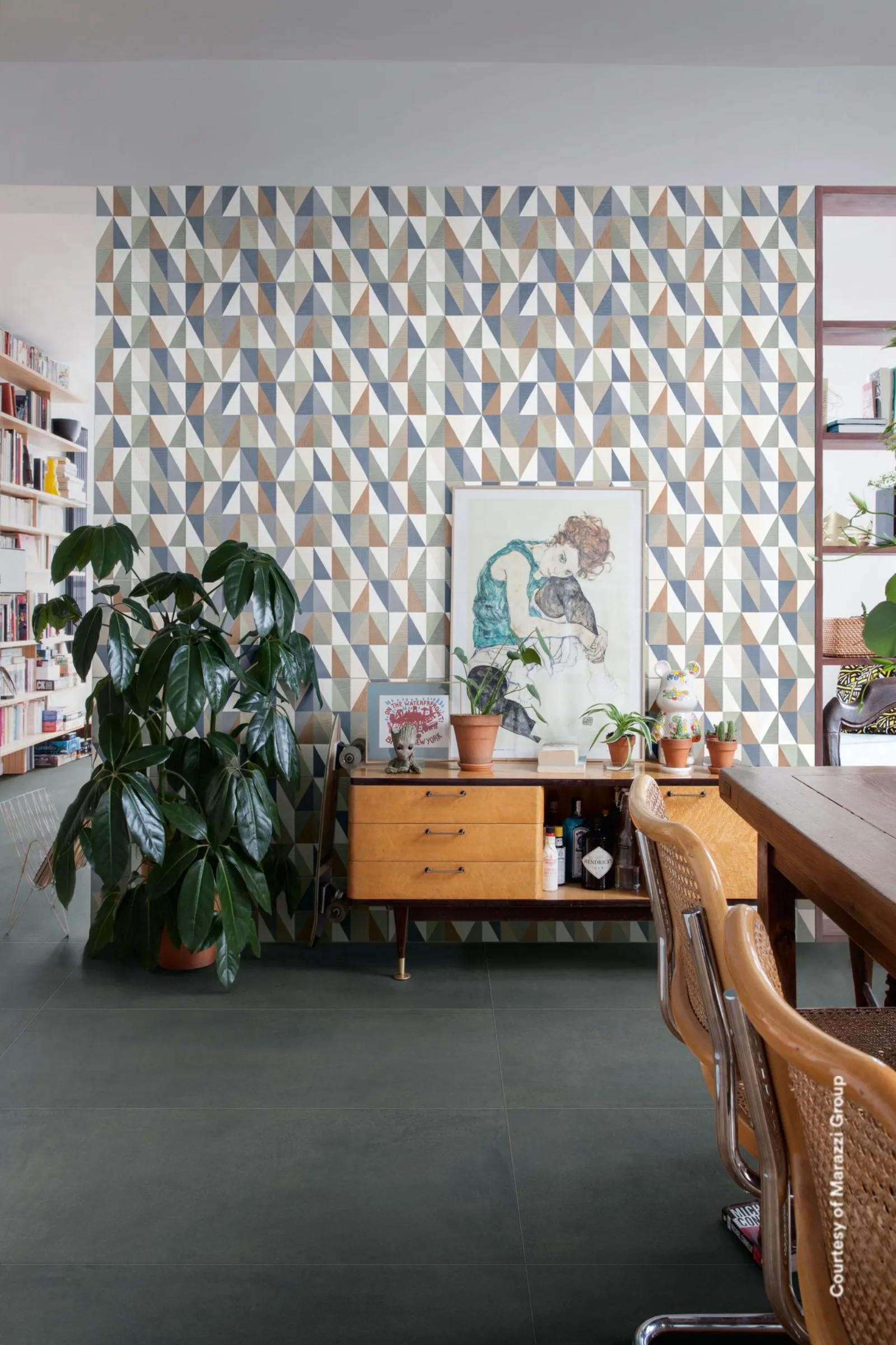 Arbeitszimmer mit Bücherregalen, Sideboard und geometrisch gemusterter Wand auf blaugrauem Betonoptik-Boden.