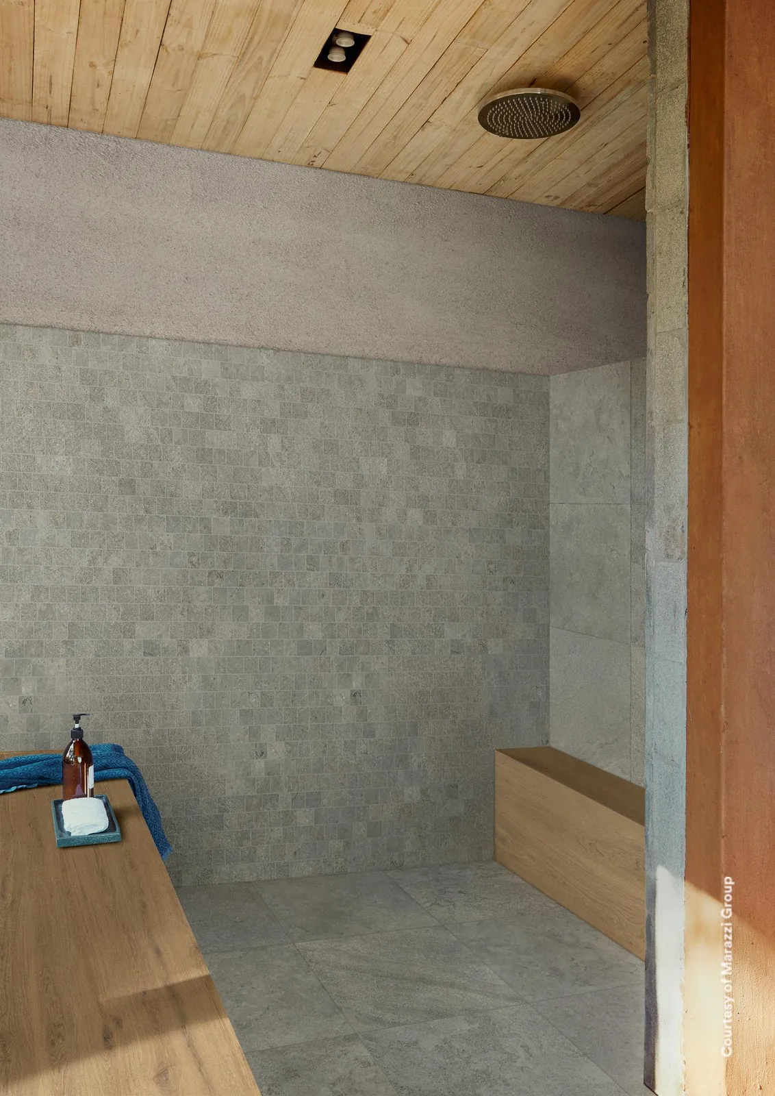 Dusche mit grauem Mosaik aus versetzten Rechteckstücken an der Wand, graue Steinoptik-Bodenfliesen und Holzbank